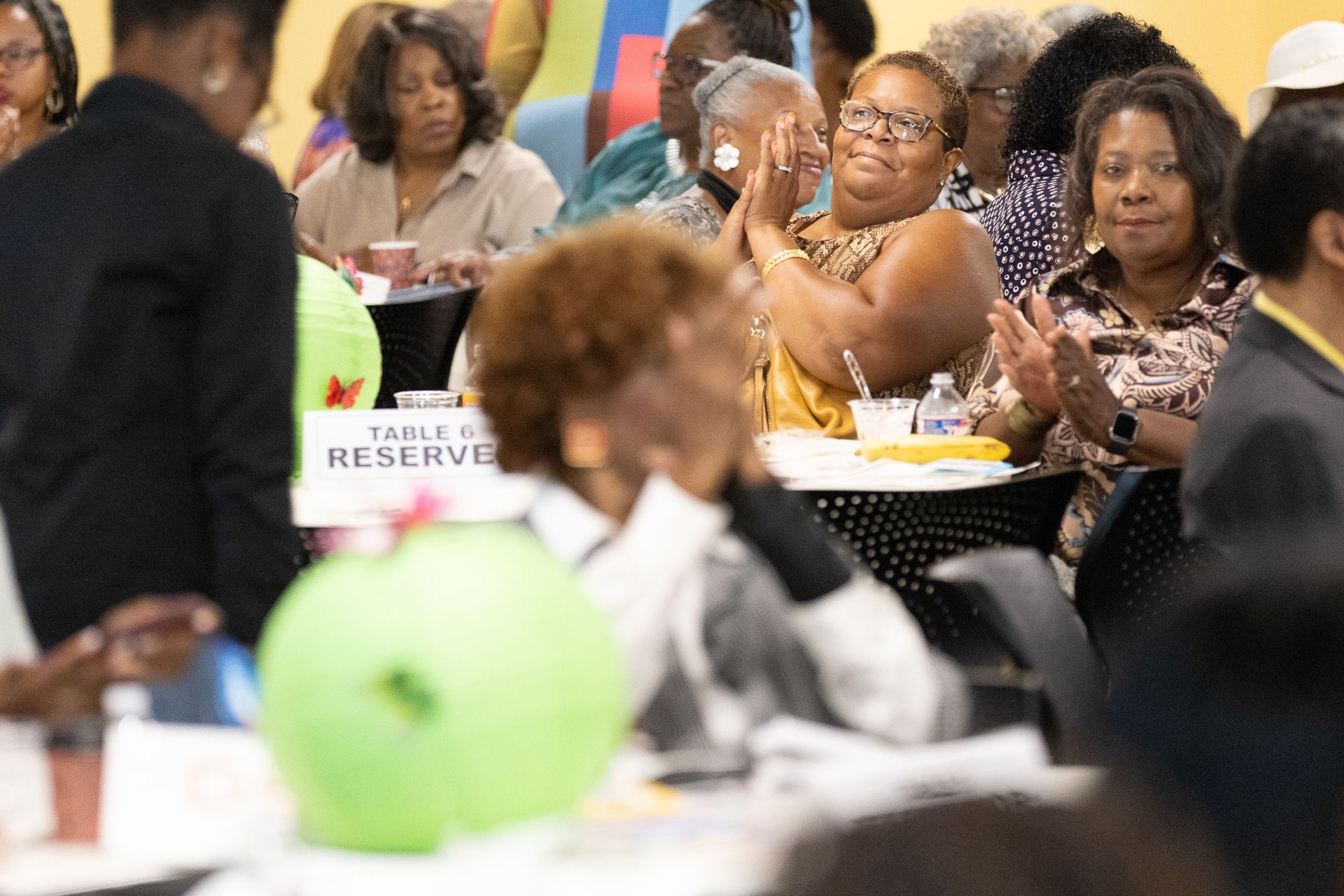 People clapping at an event, seated at tables with reserved signs.