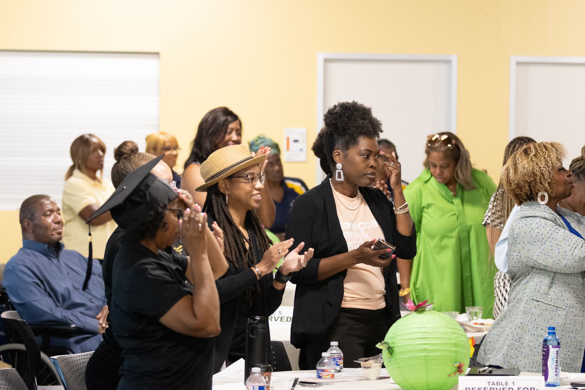 People clapping in a light-yellow room, some looking at their phones. 