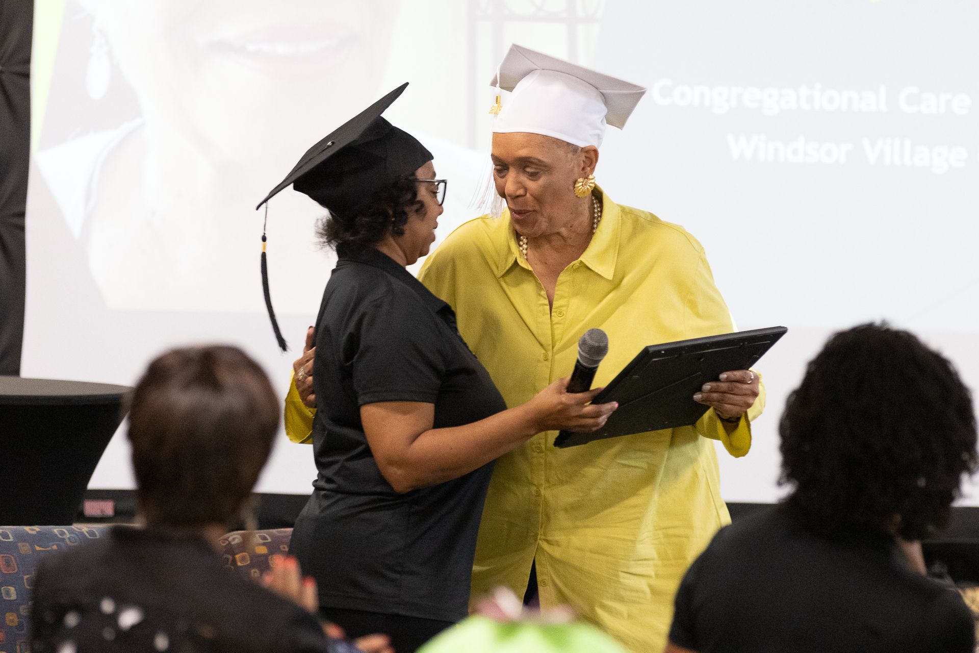 Two people in graduation caps at a ceremony, one receiving a diploma.