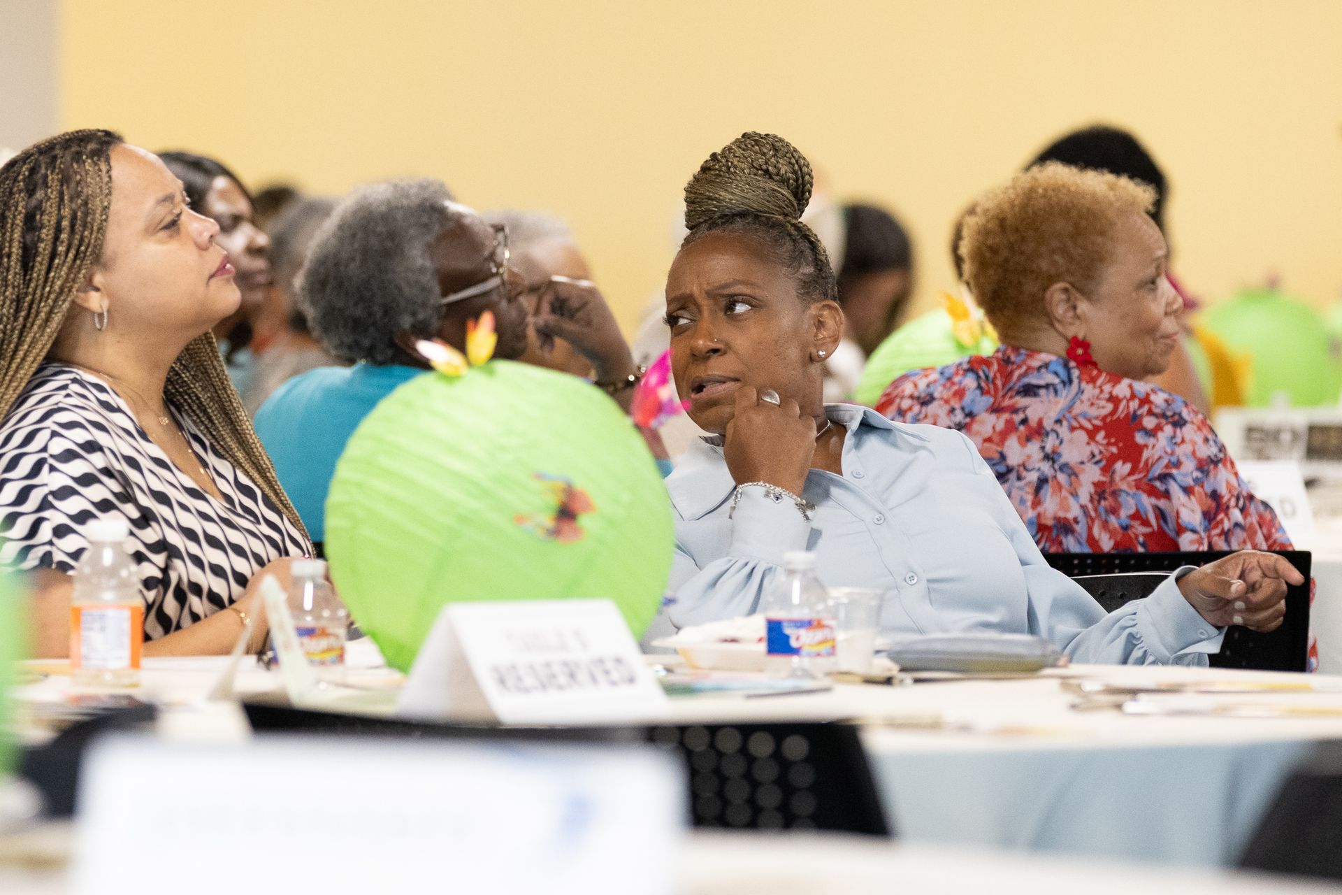 Attendees listen attentively at a conference table, some with thoughtful expressions, lit by overhead lights.