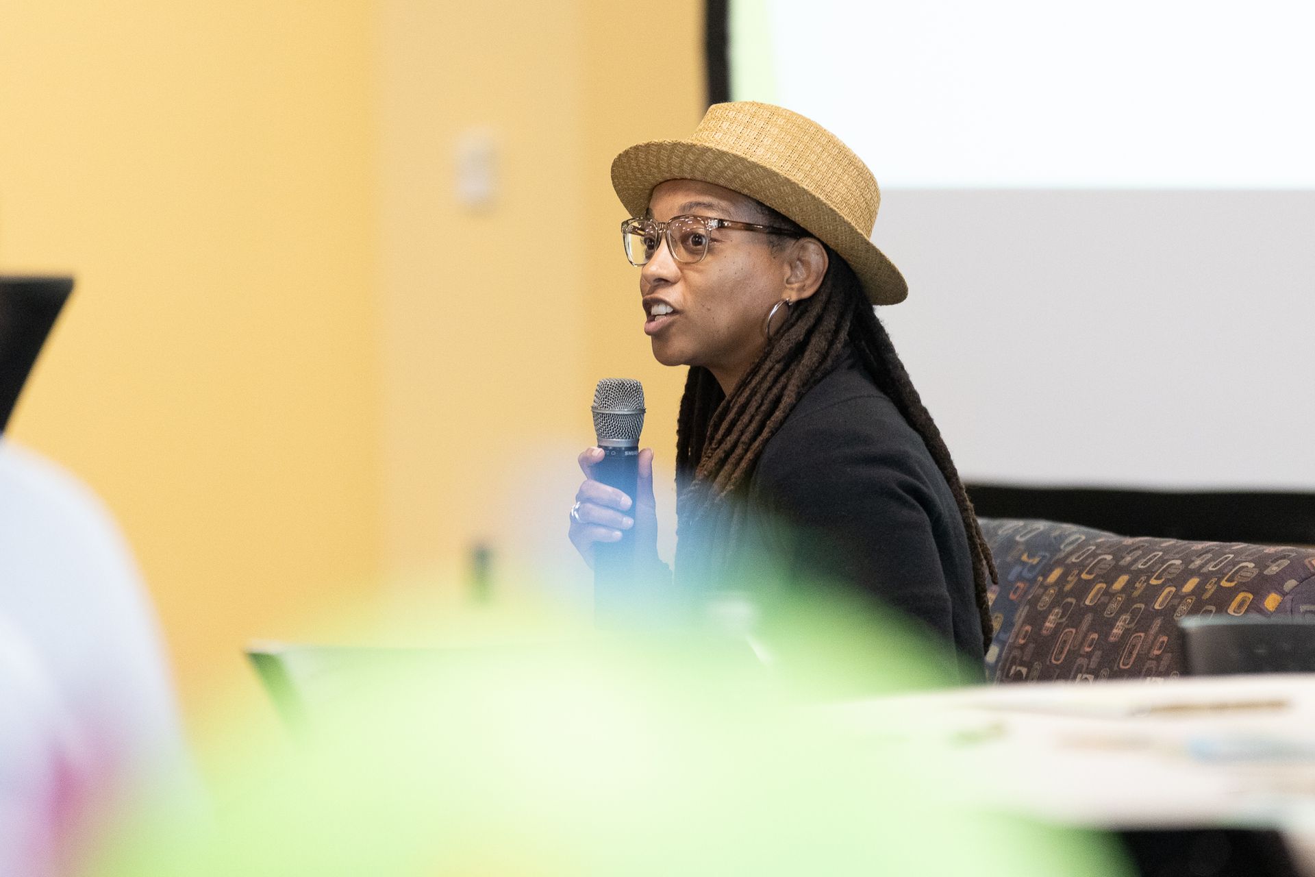 Woman in straw hat speaks into microphone at a conference.