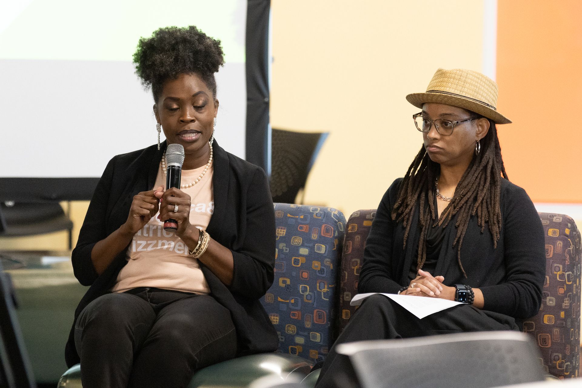 Two women at a panel discussion. One speaks into a microphone, the other looks on, holding notes.