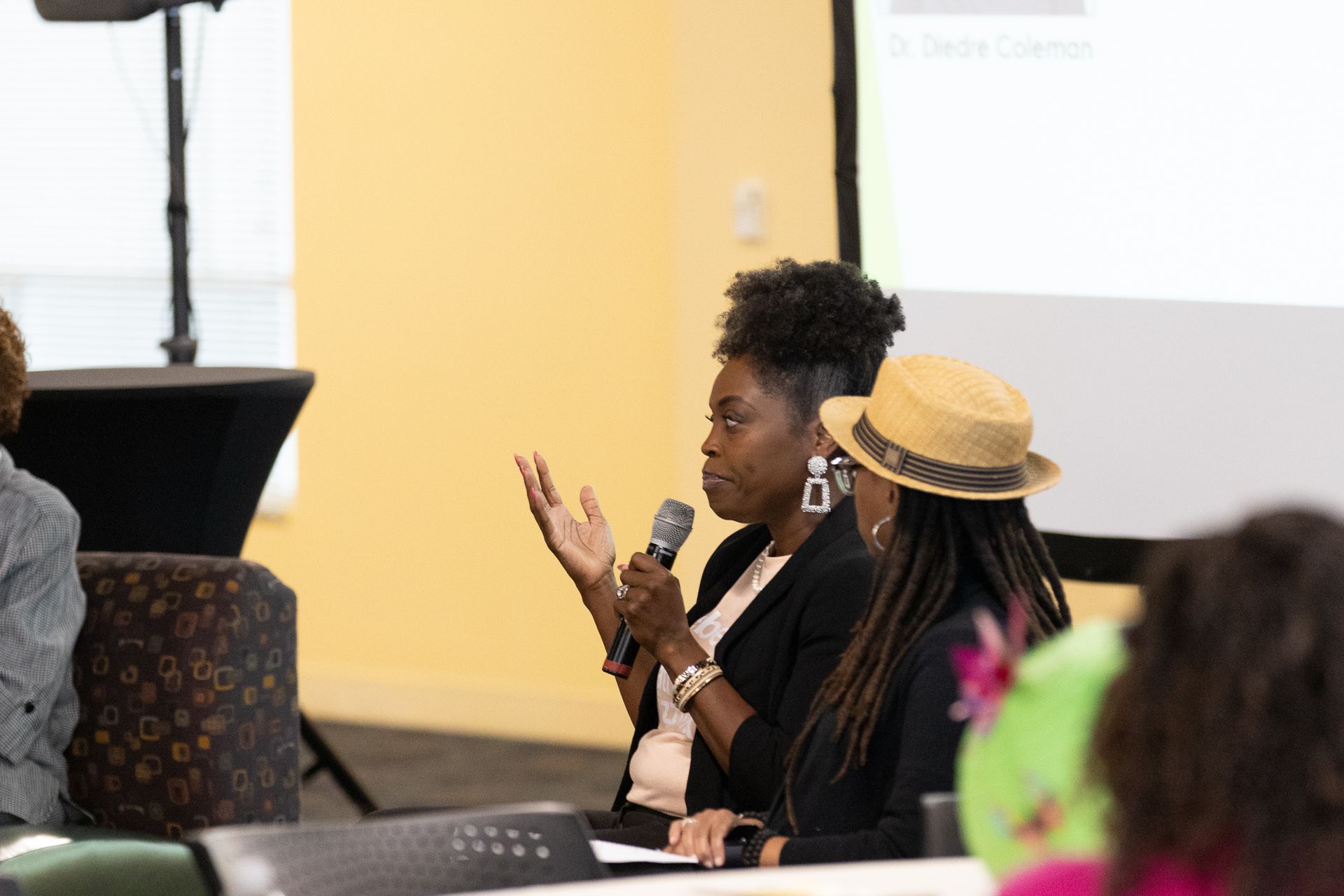 Two women speaking at a panel discussion, one holding a microphone, facing the audience.
