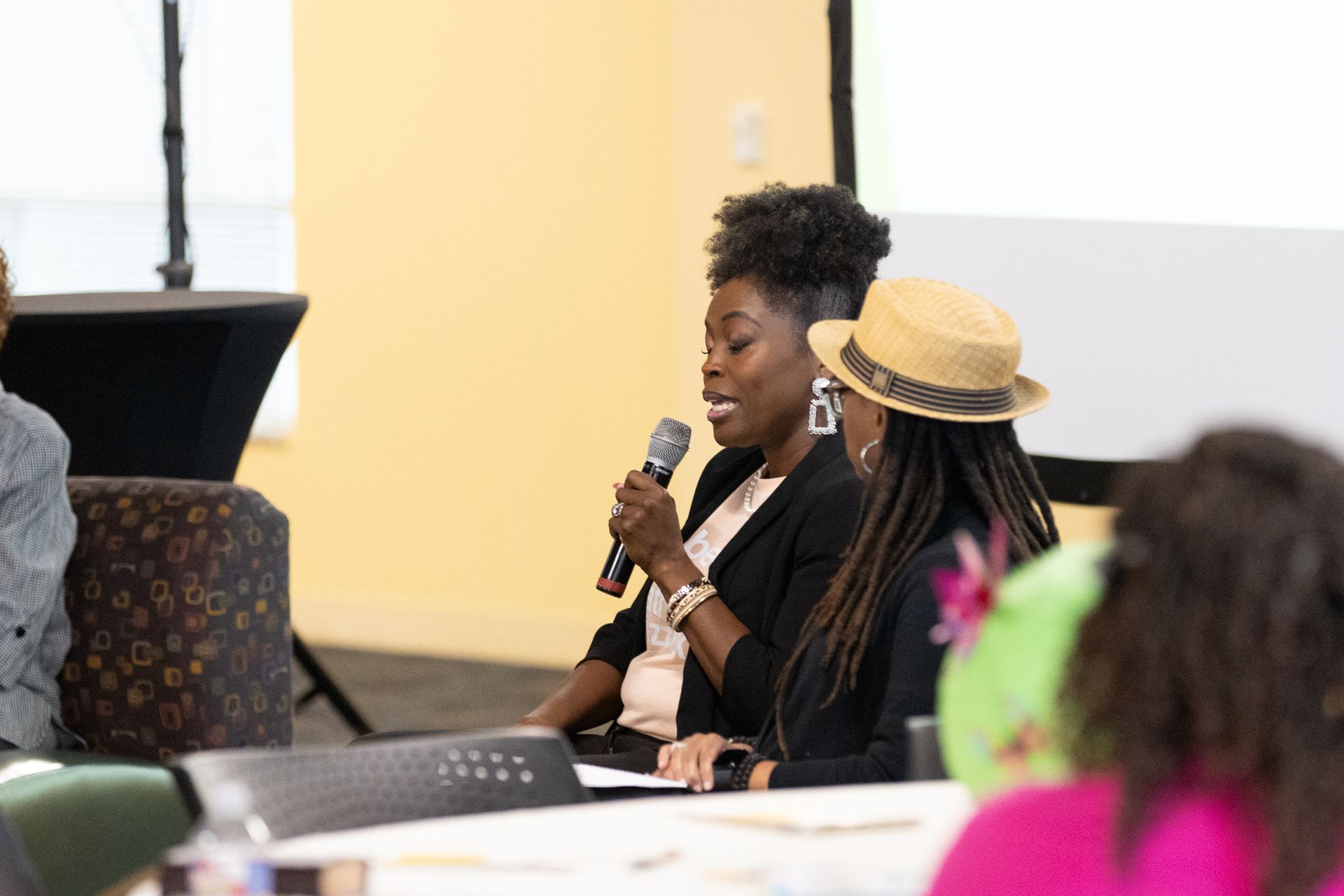 Woman speaking into a microphone during a panel discussion; another woman sits beside her.