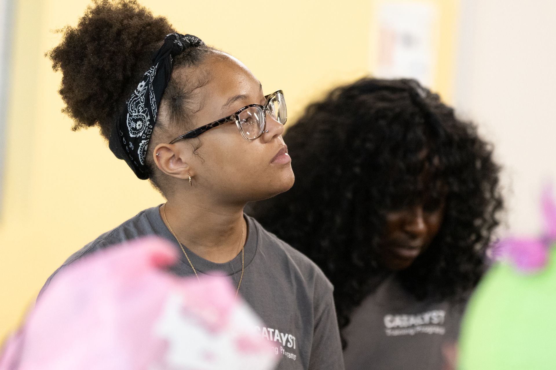 Woman in glasses and bandana looks upward; another woman in the background.