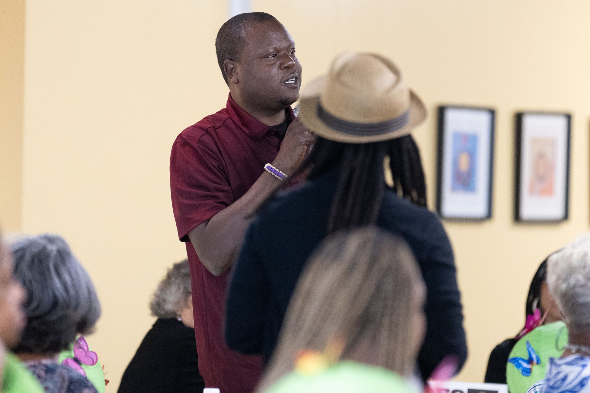 Man speaks to another person in a room, a group of people in the foreground listen.