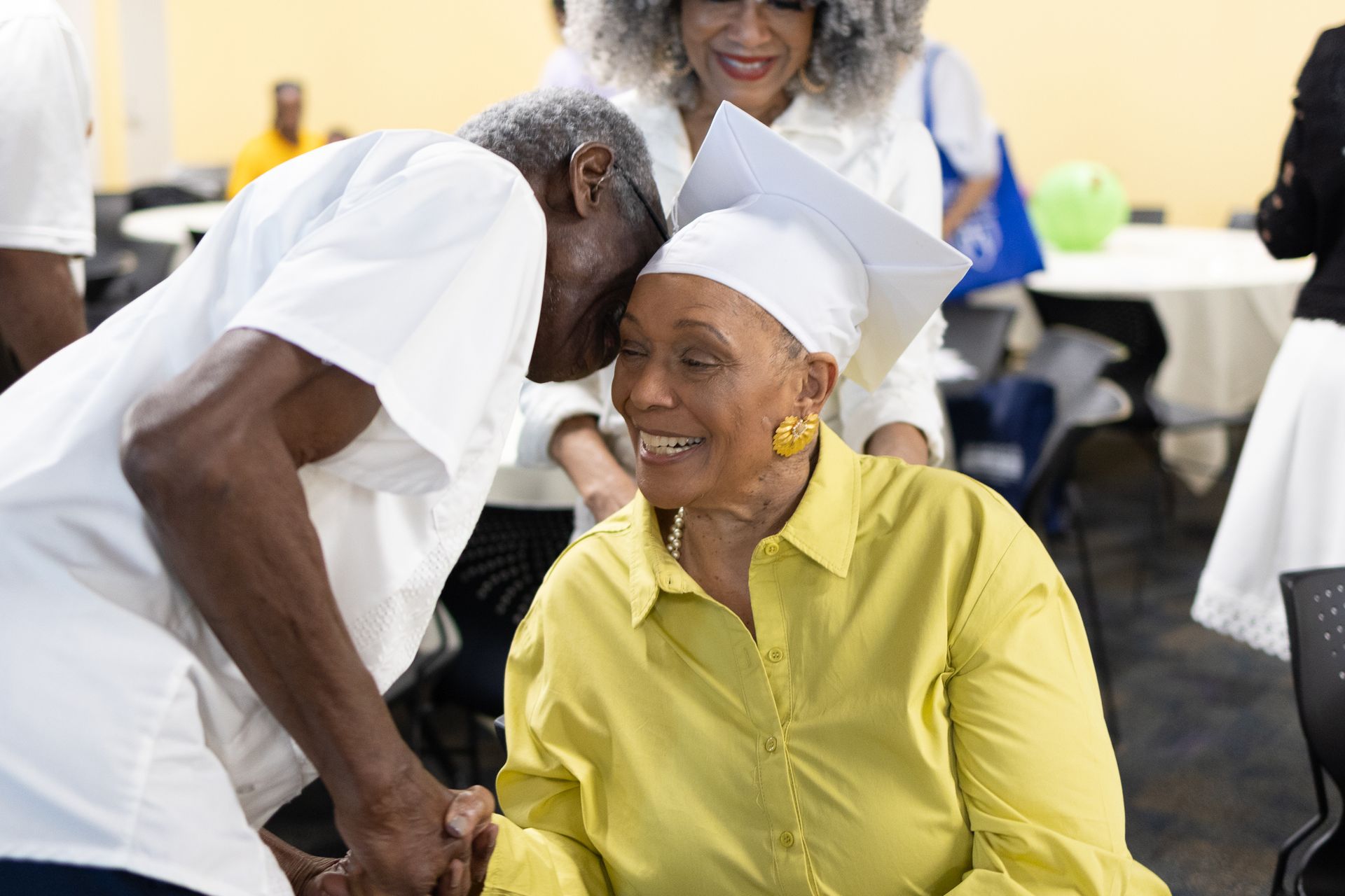 Man leans in to congratulate woman in graduation cap and yellow shirt.
