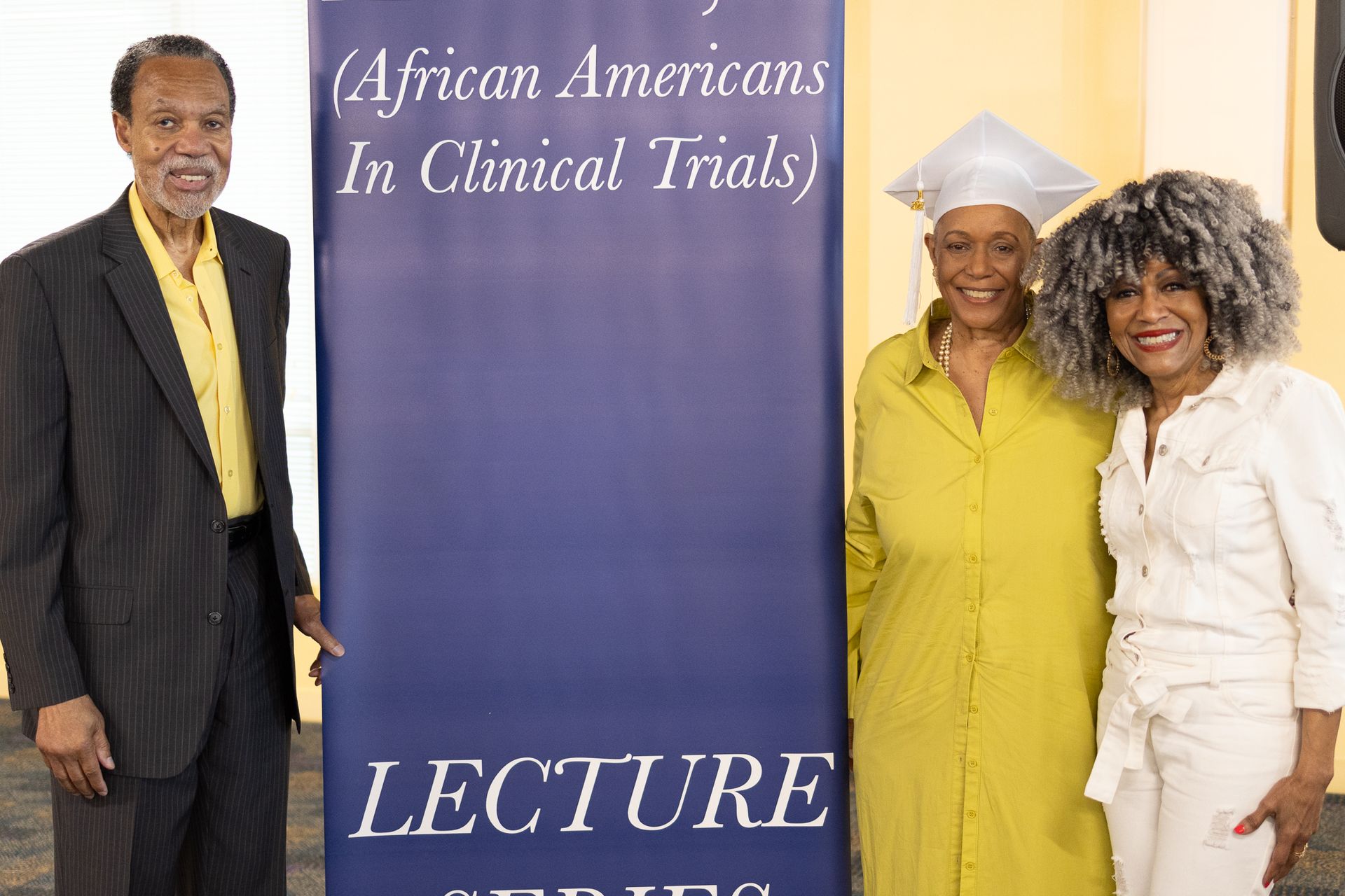 Three people stand next to a lecture series banner. The banner reads 