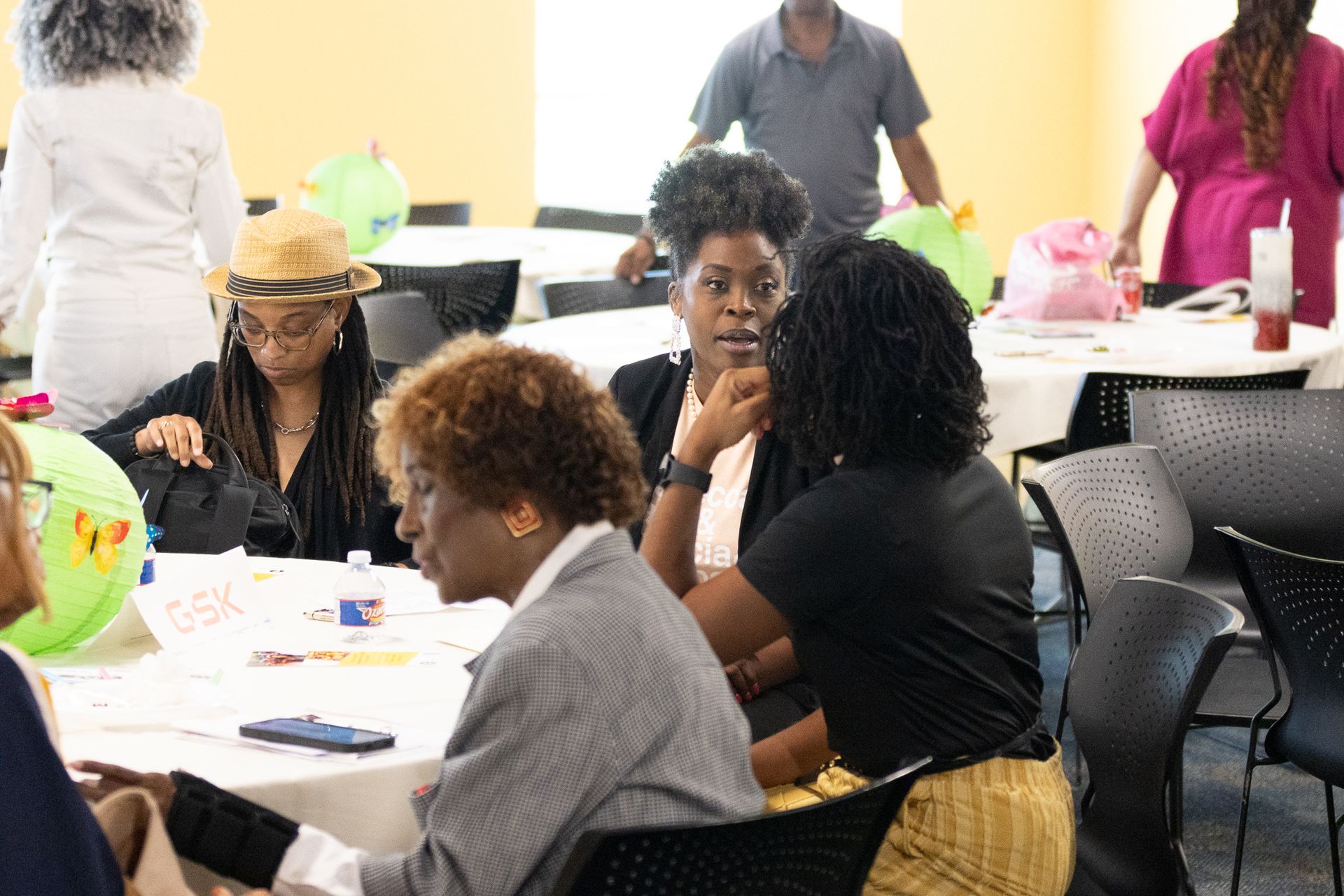 People seated around tables in a room with a casual gathering; some are talking, others looking.