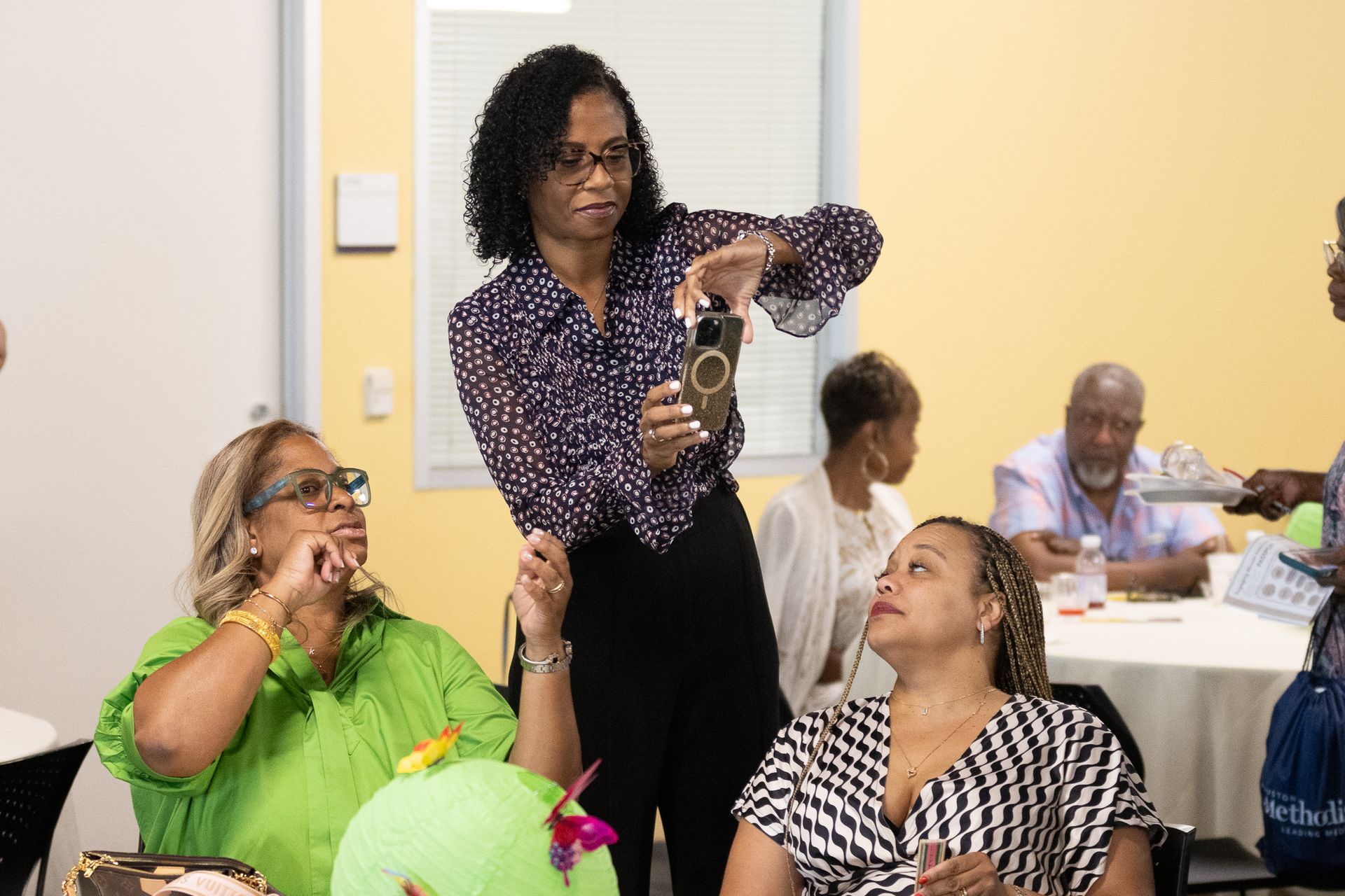 Woman taking a photo of others at a table. People are seated in a well-lit room with yellow walls.