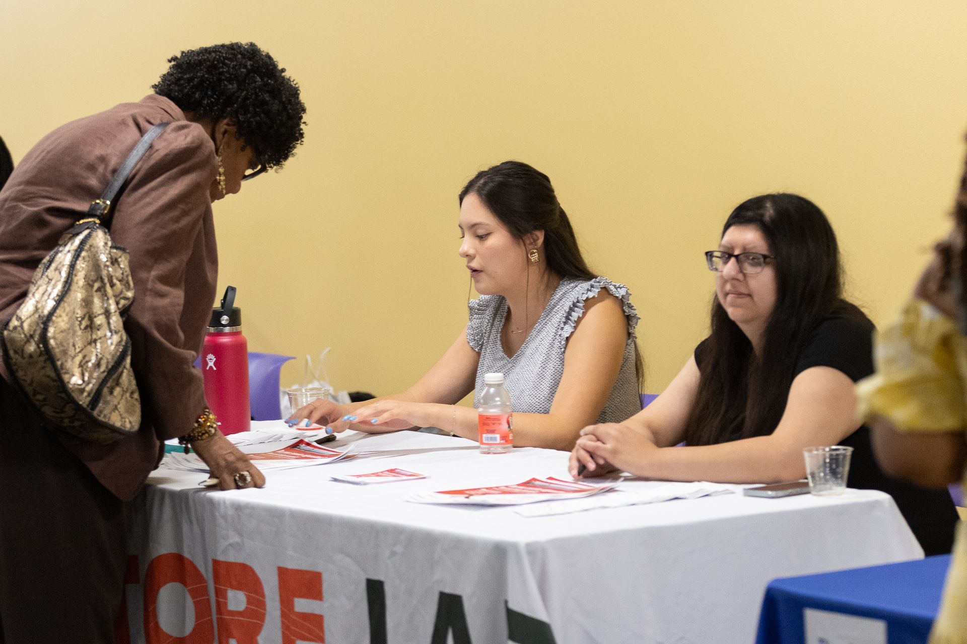 Woman at information table speaks with two others. Table with 