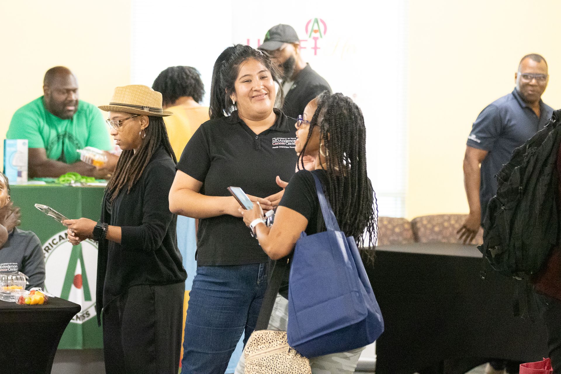 People networking at an event. Woman smiles and talks, holding a phone. Others converse and mingle.