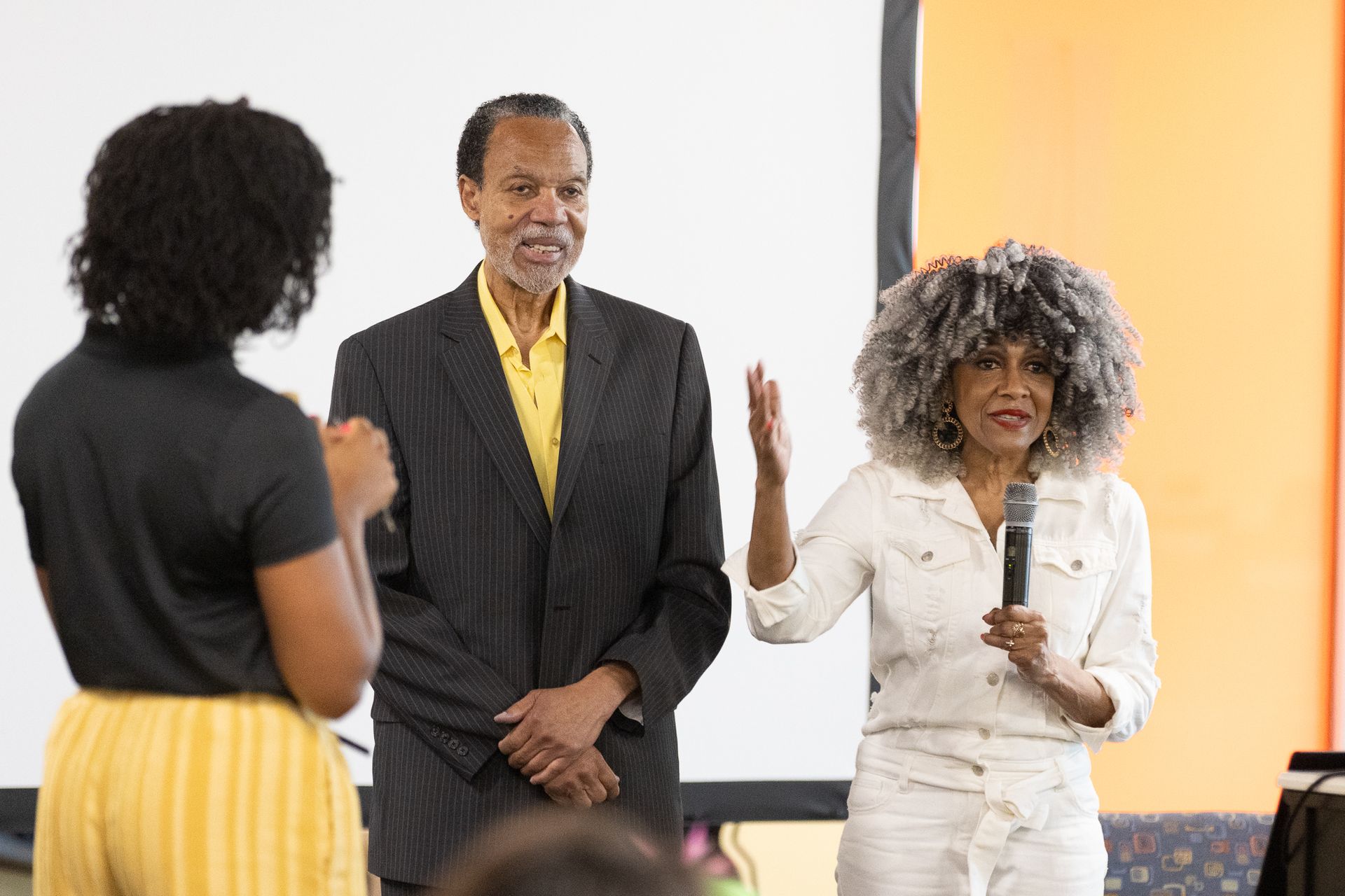 Woman speaks into mic with others on stage.