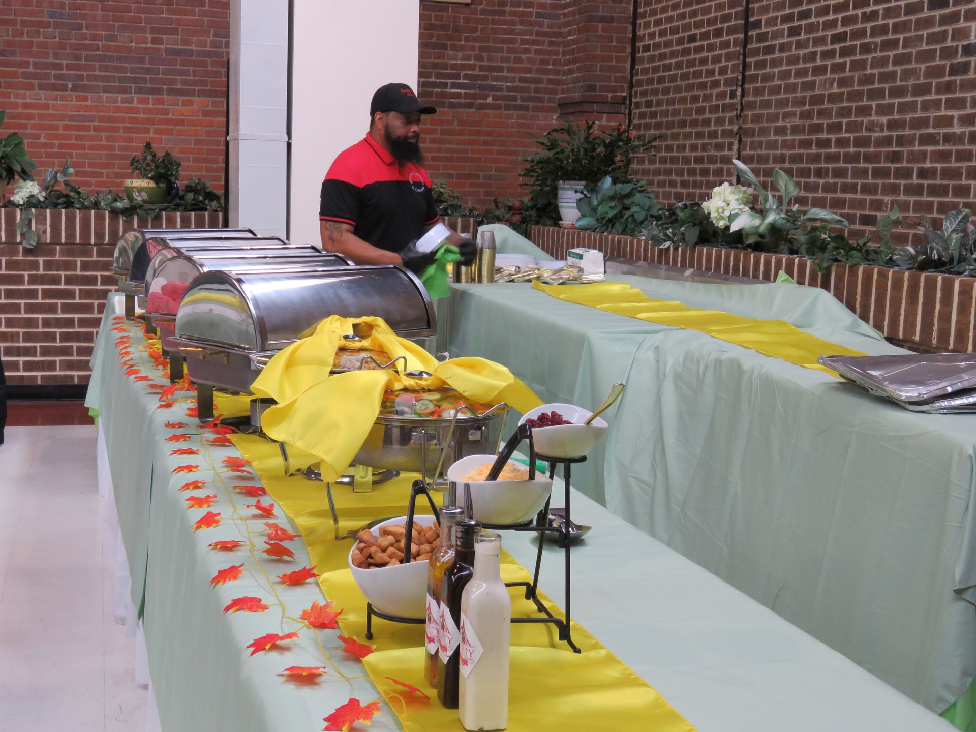 Buffet table with catering staff. Yellow runners on green tablecloths; stainless chafing dishes, autumn decor.