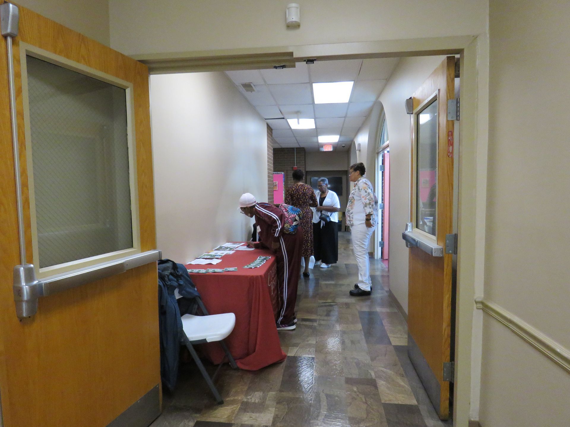 Hallway with people near a table with materials. One person in white and others in maroon and black.
