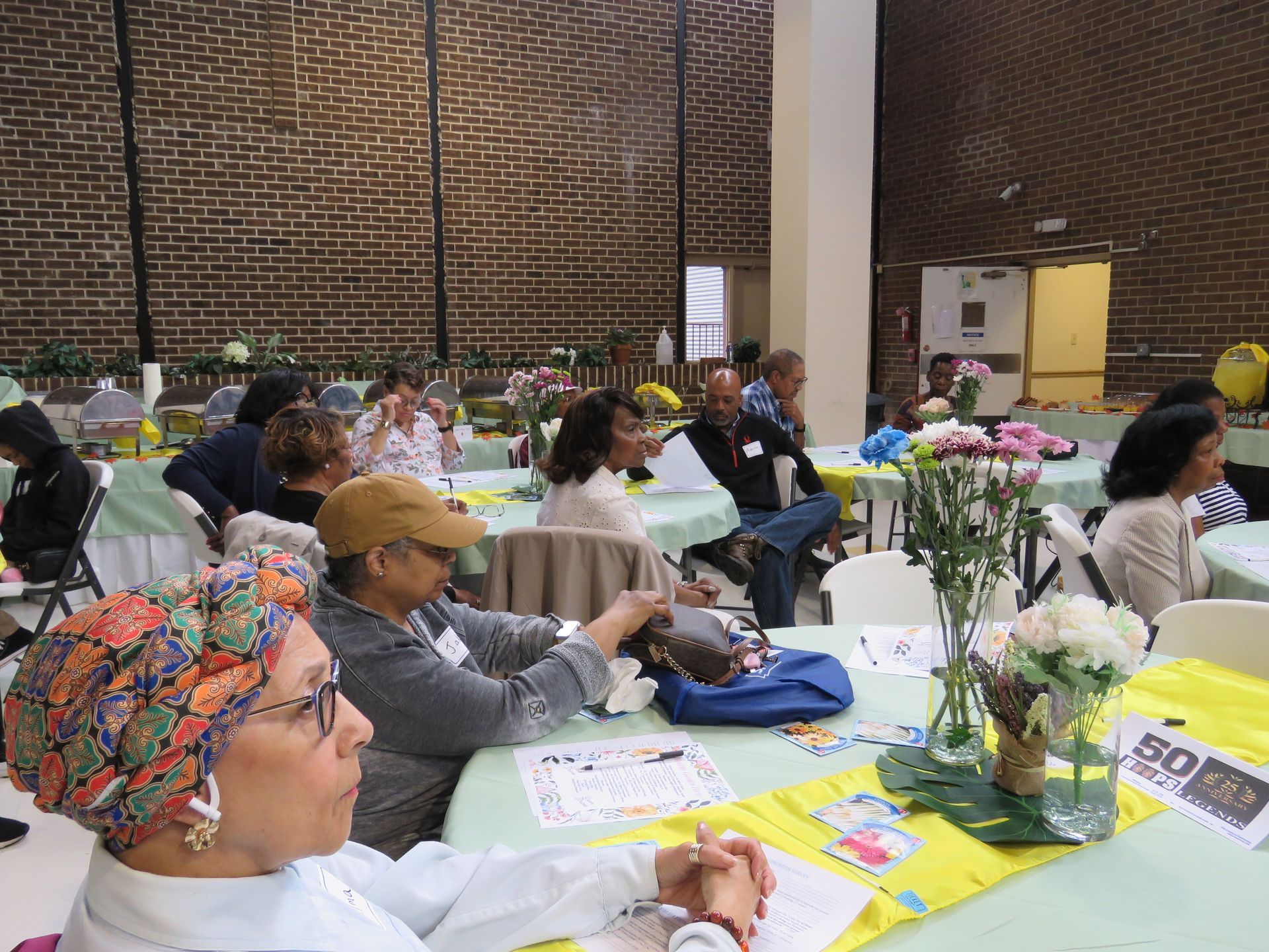 People seated at tables in a room with a brick wall, some with flowers and decorations.