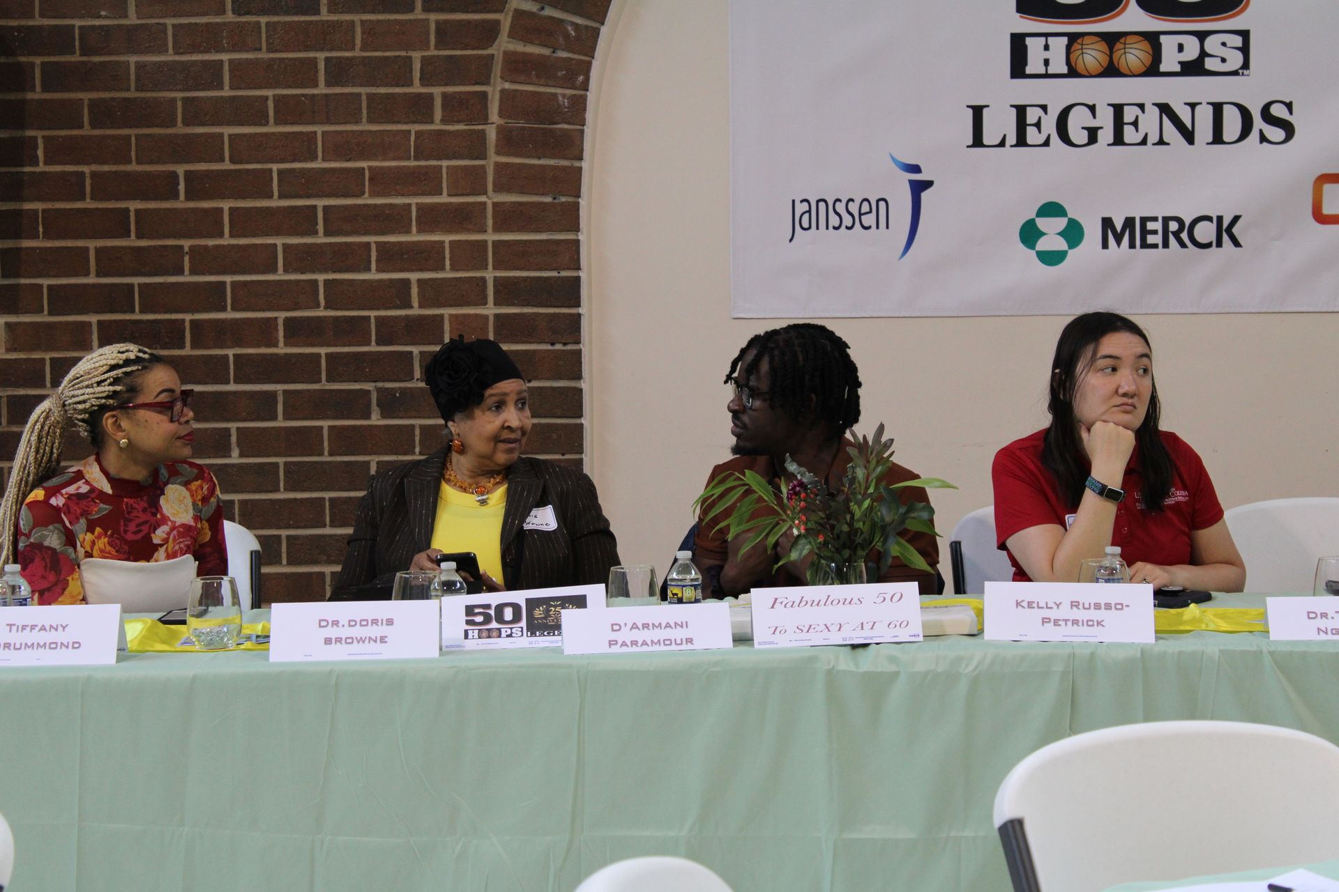 Panel of four women seated behind a table, speaking at an event with sponsors.