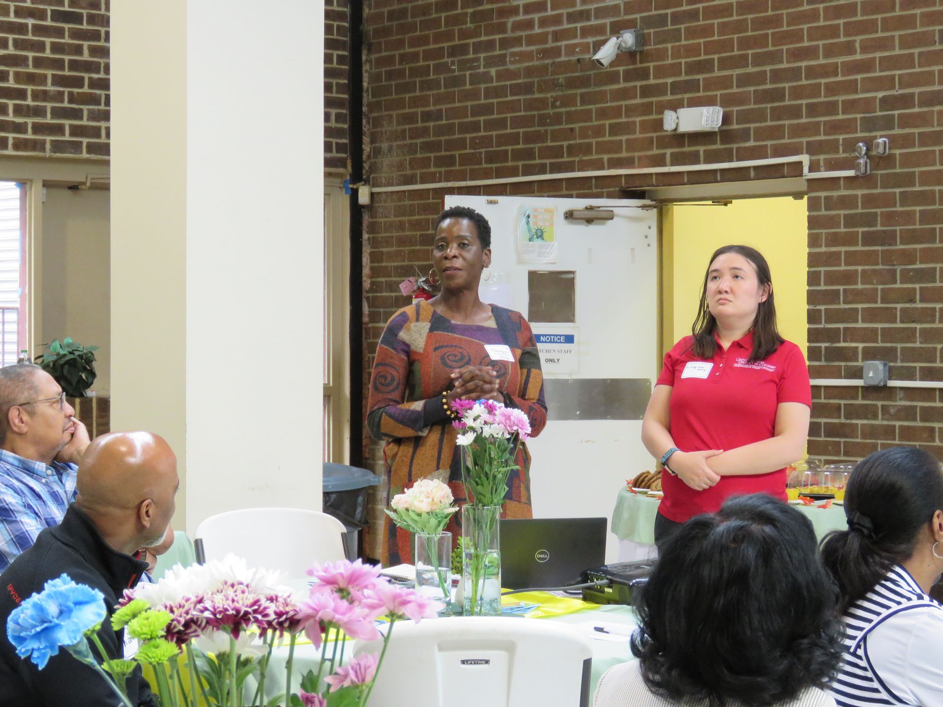 Two women present at a community event, standing by a table with flowers.