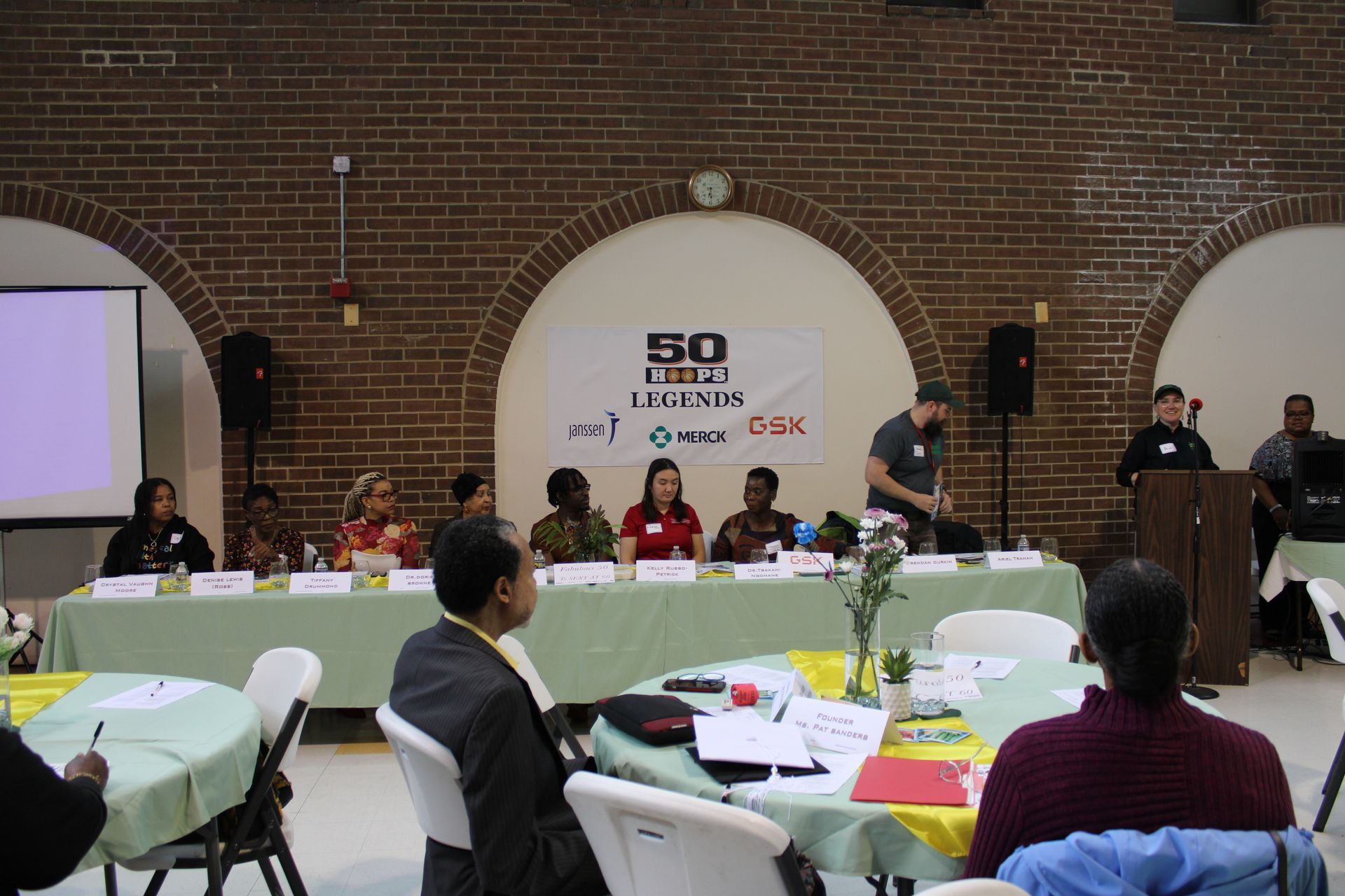 Panel discussion at a community event. People seated behind a long table, speaker at a podium.