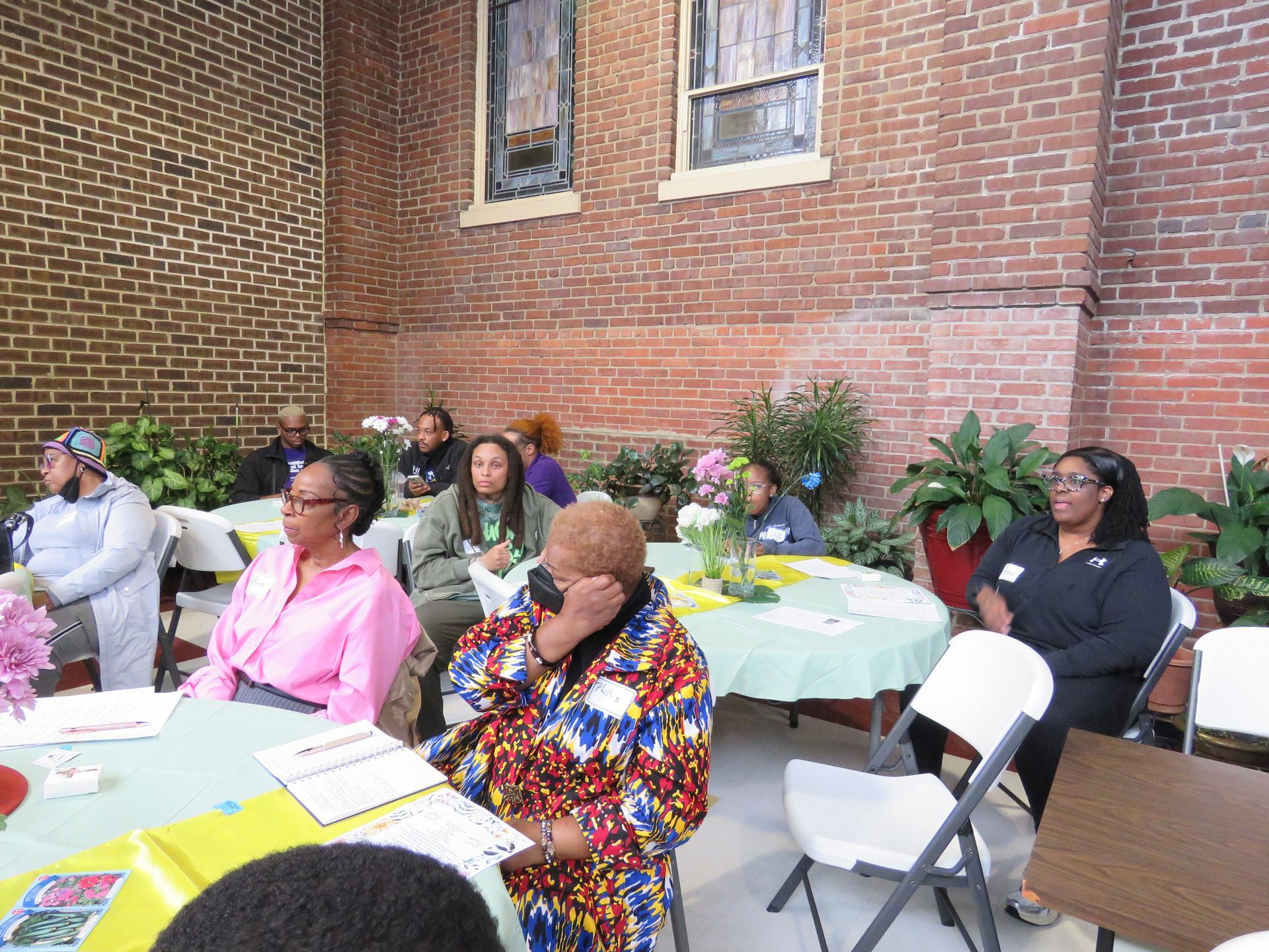 People seated around tables in a brick-walled outdoor setting, possibly a gathering or meeting.