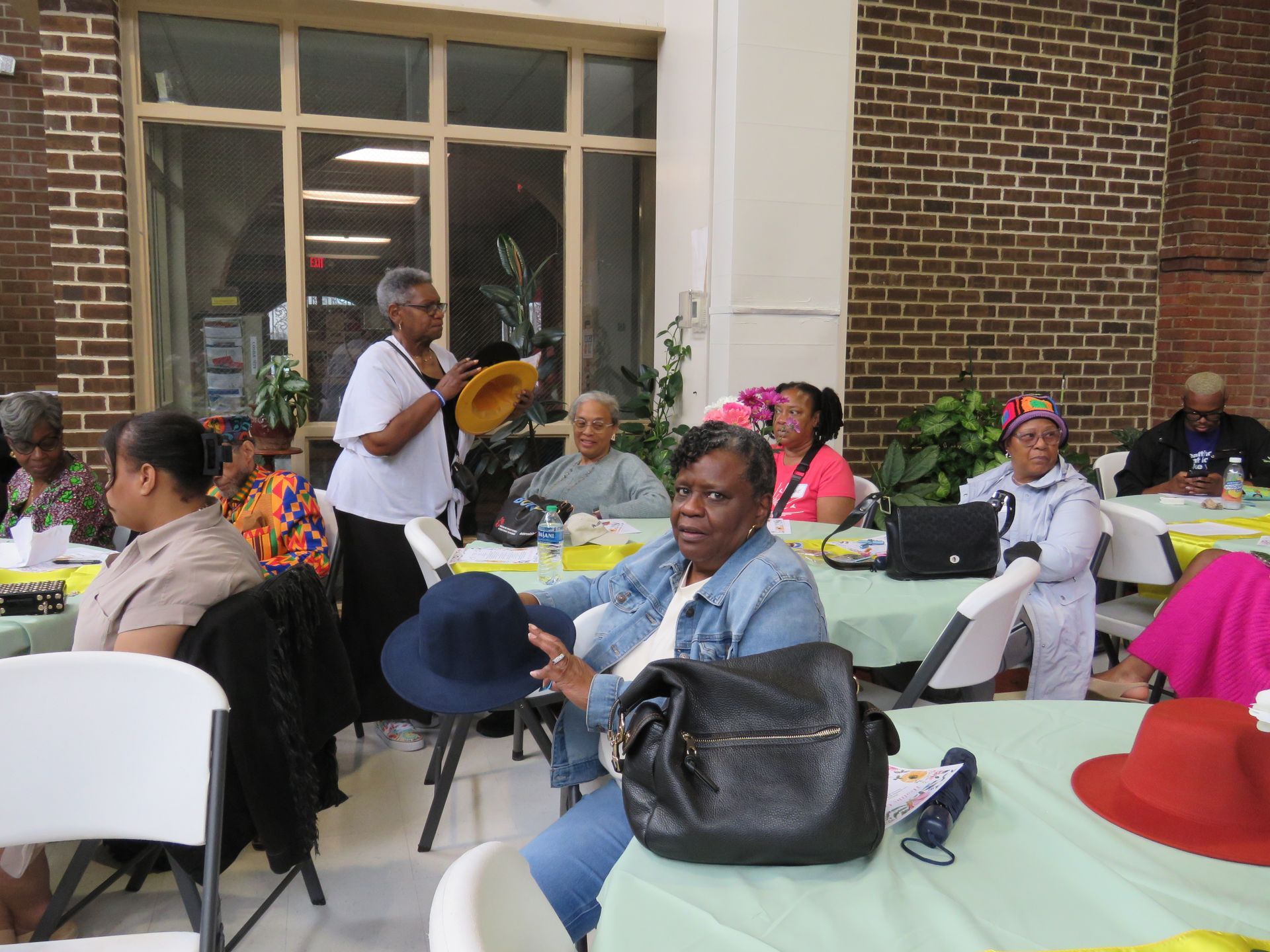People gathered at tables, one woman holding a hat, indoors.