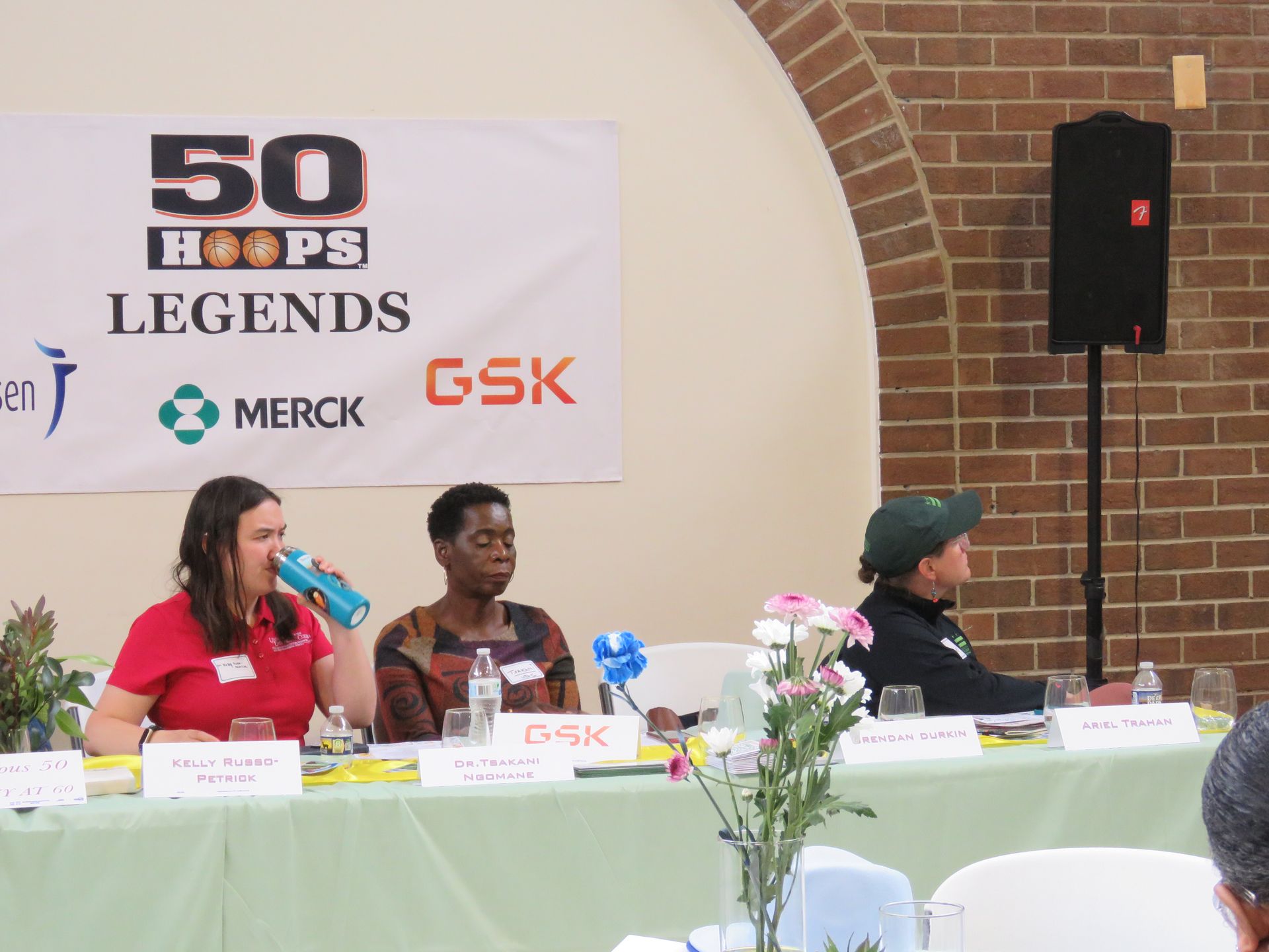 Panel discussion with three speakers at a table, banner behind them reads 