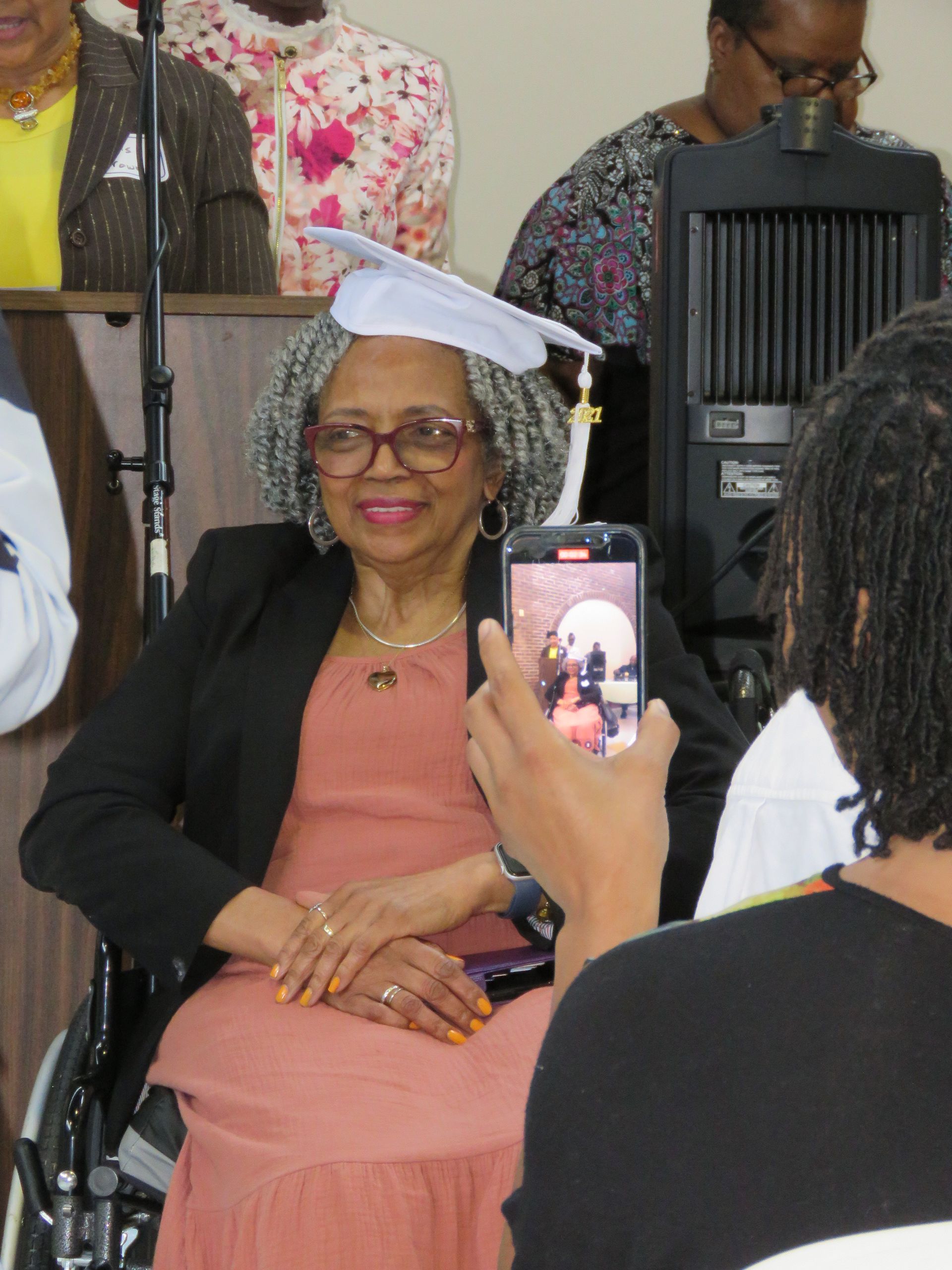 Woman in graduation cap and gown in wheelchair, being photographed.