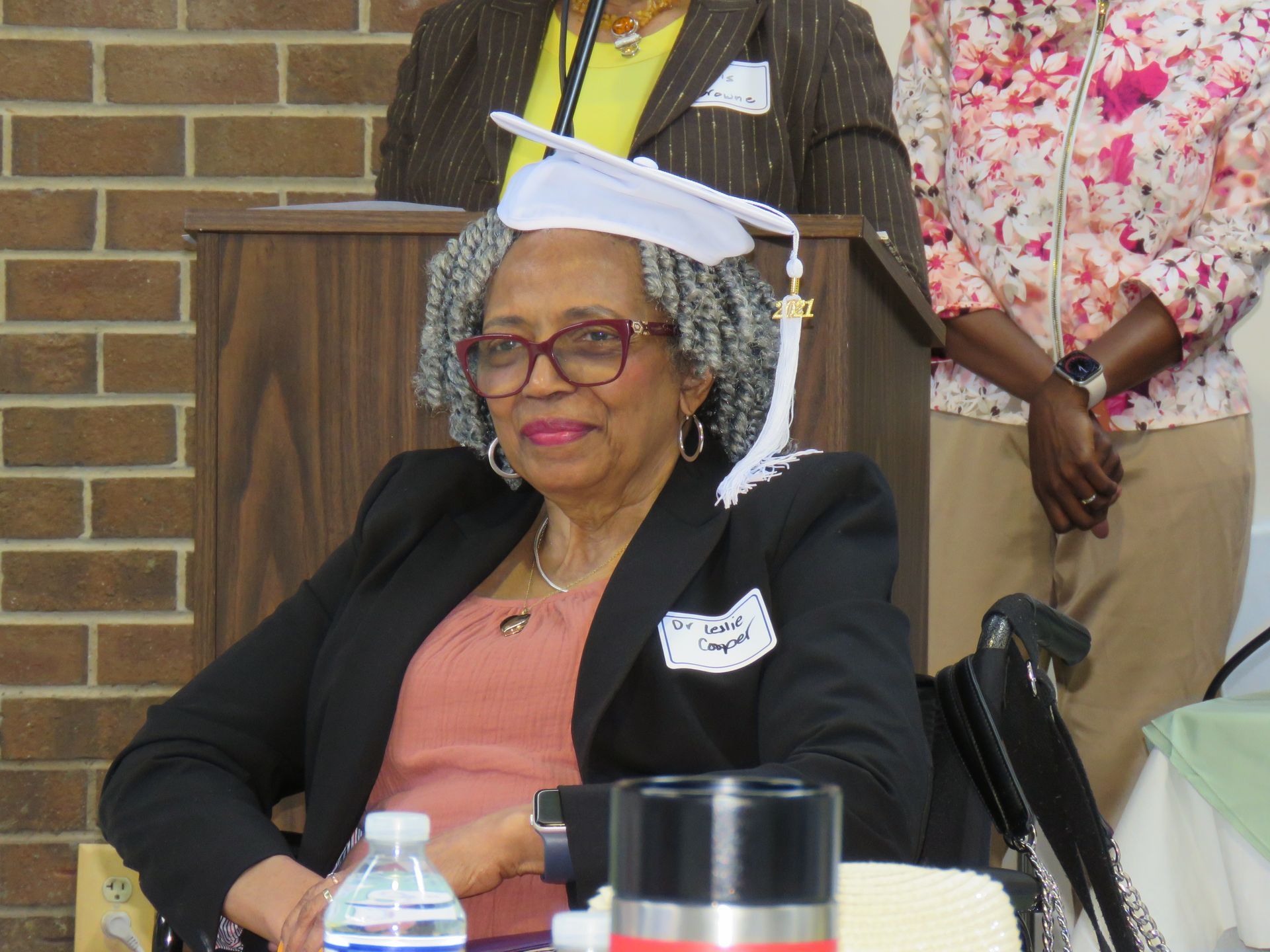 Woman in graduation cap smiles at podium.