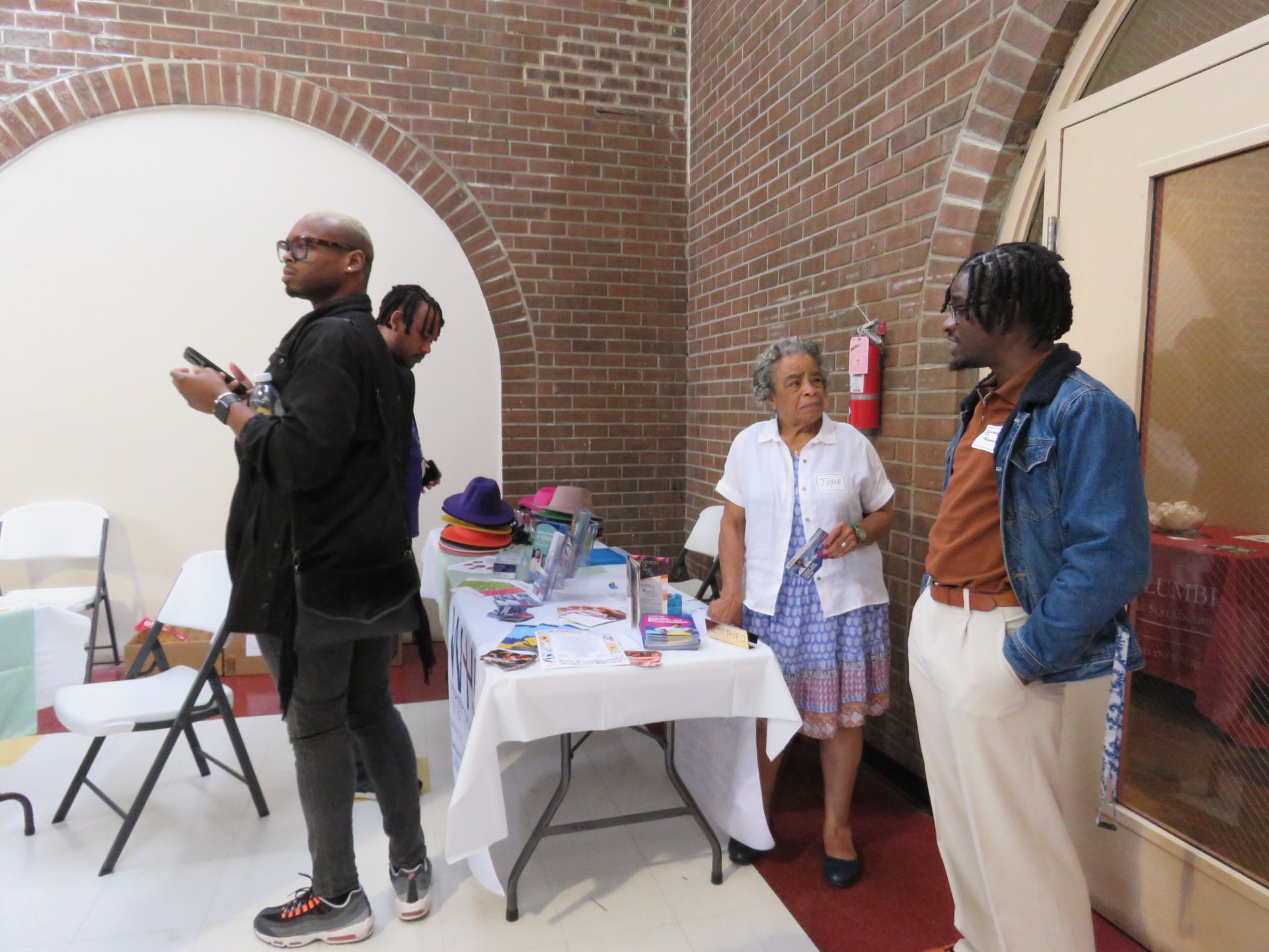 People standing near a table with materials in a room with brick walls.