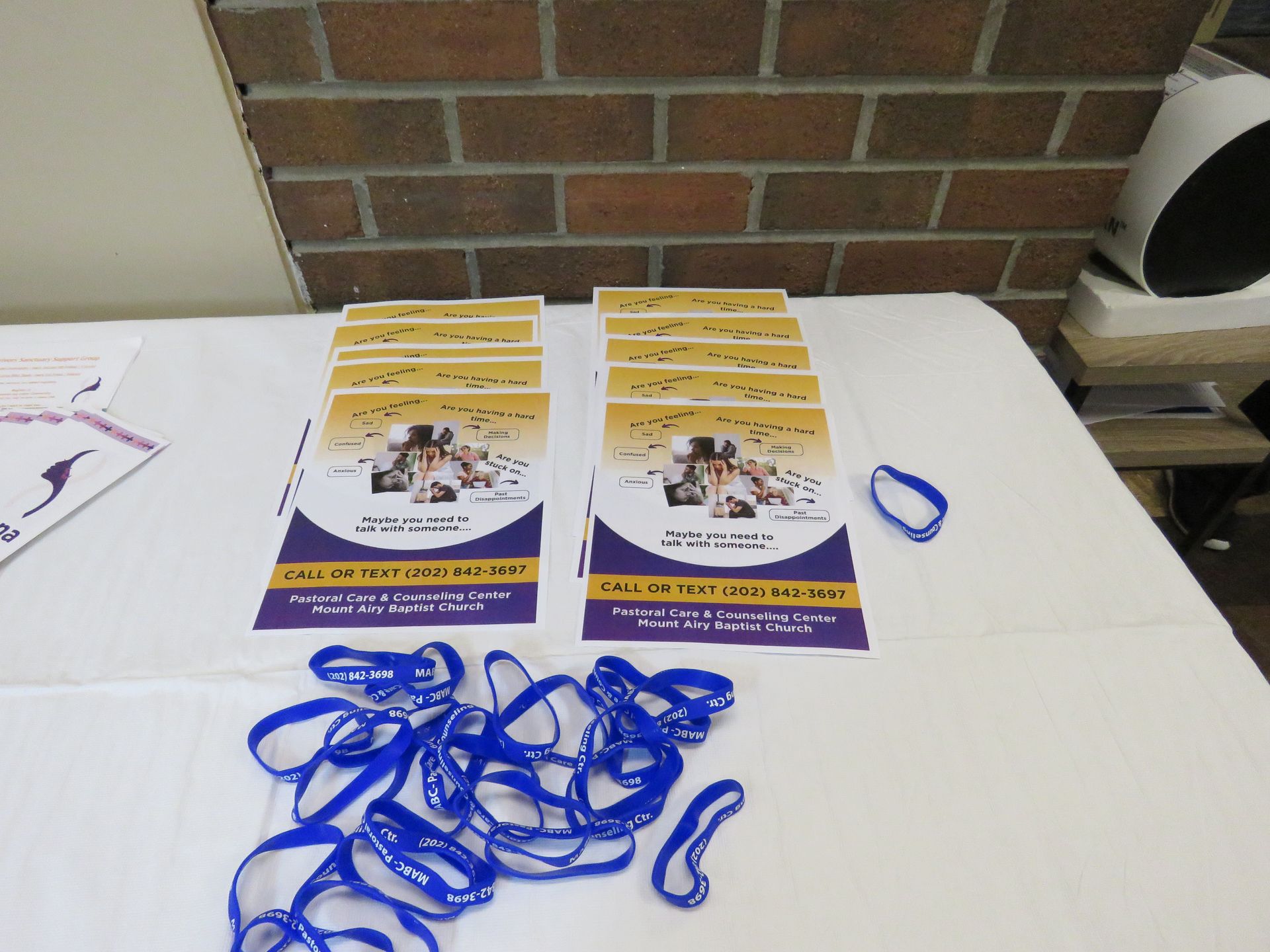 Table with stacked brochures, blue wristbands, against a brick wall.