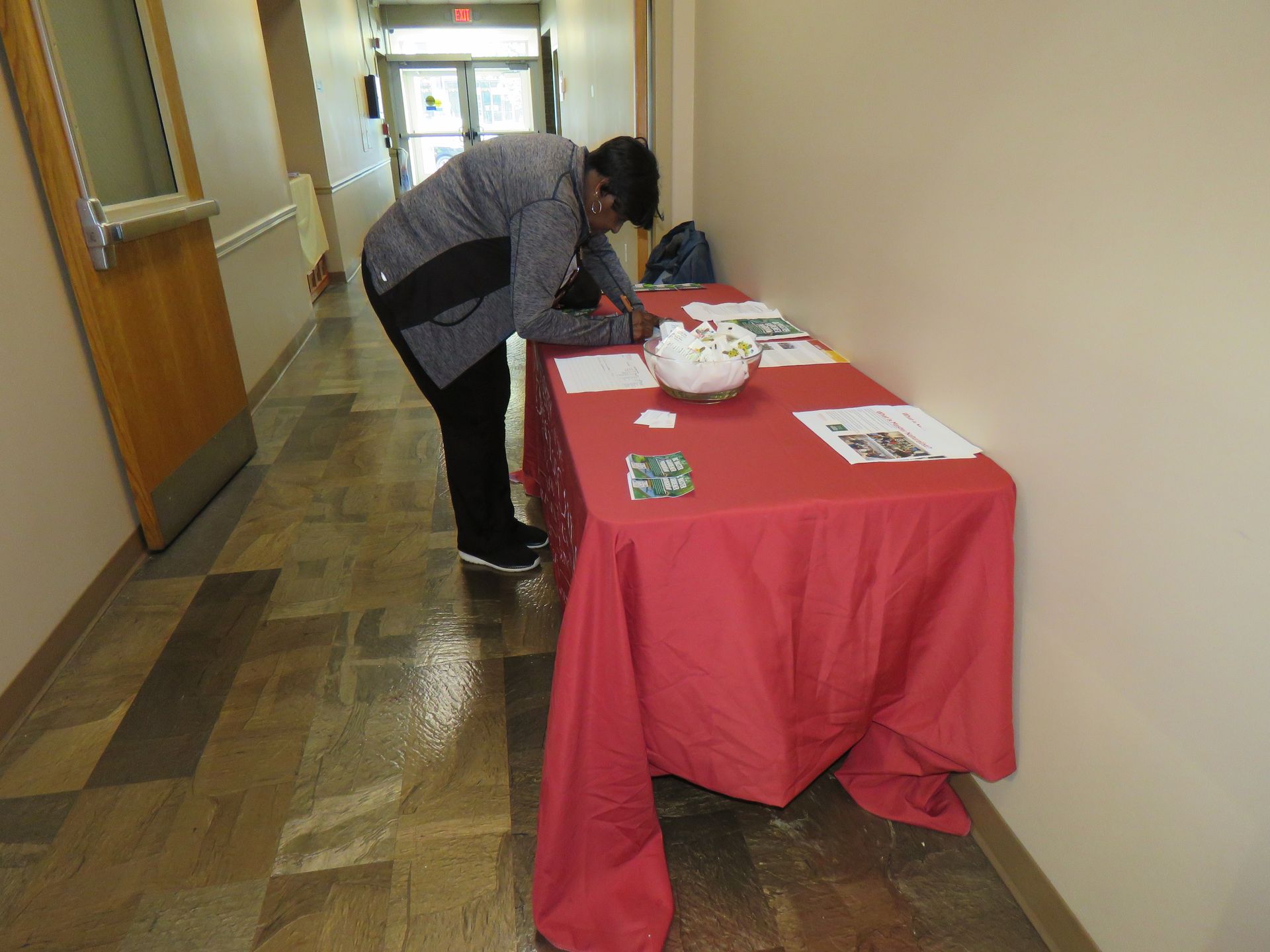 Person signing a document on a red-covered table in a hallway.