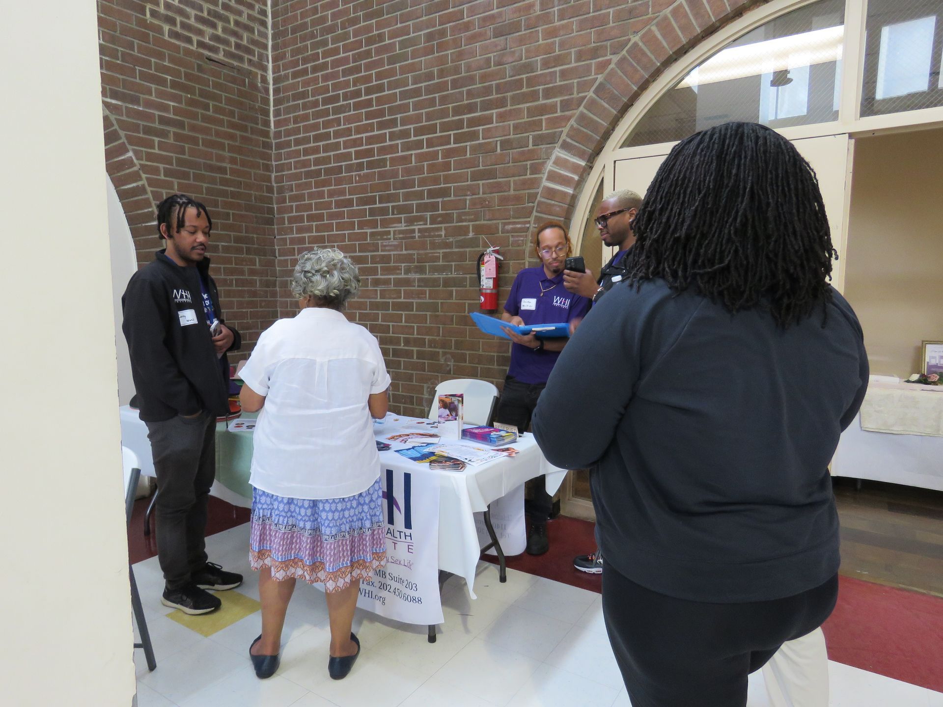 People at a table with information, talking and looking at materials. Brick wall in background.