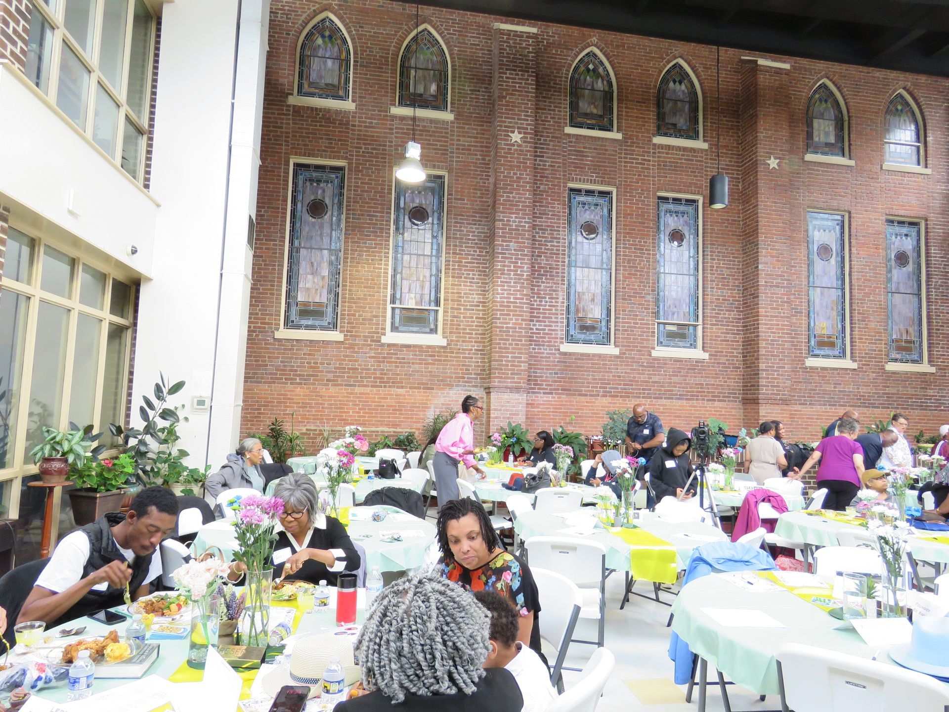 People eating at tables in a brightly lit room with decorative stained glass windows.
