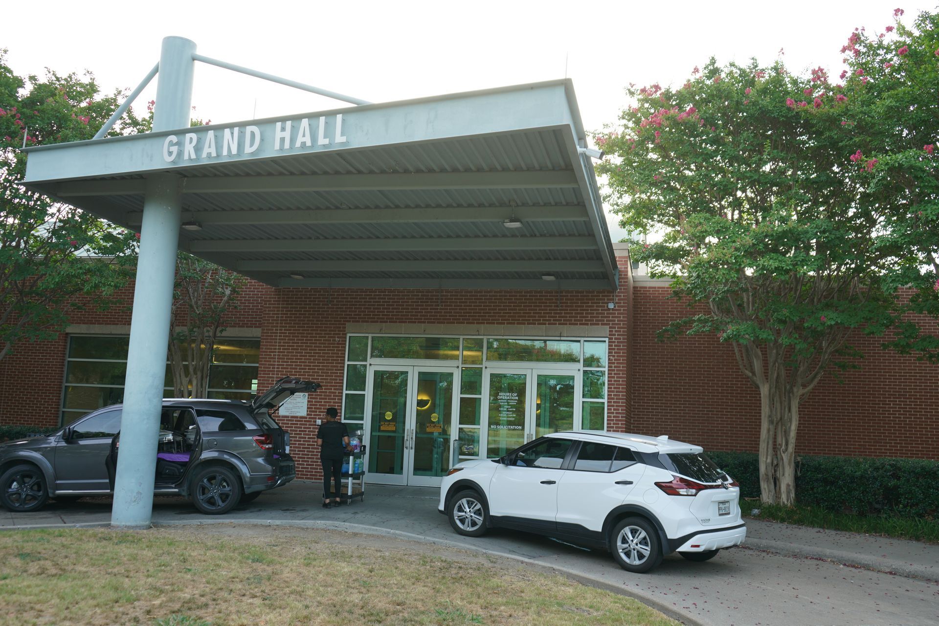 Grand Hall entrance with cars. White and gray SUVs parked under a canopy.