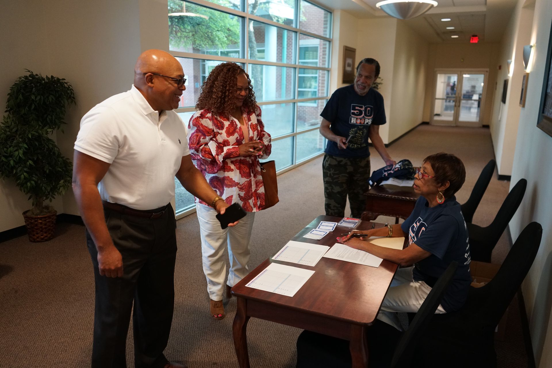 People registering at a table in a hallway. One person is seated, others standing.