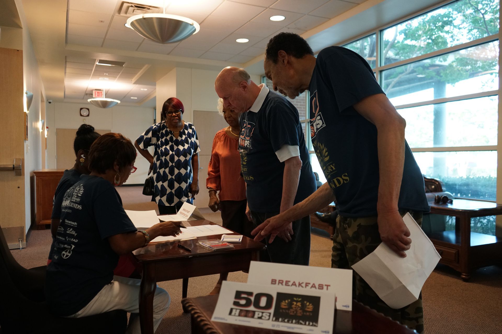 People registering at a breakfast event, standing near a table with signage.