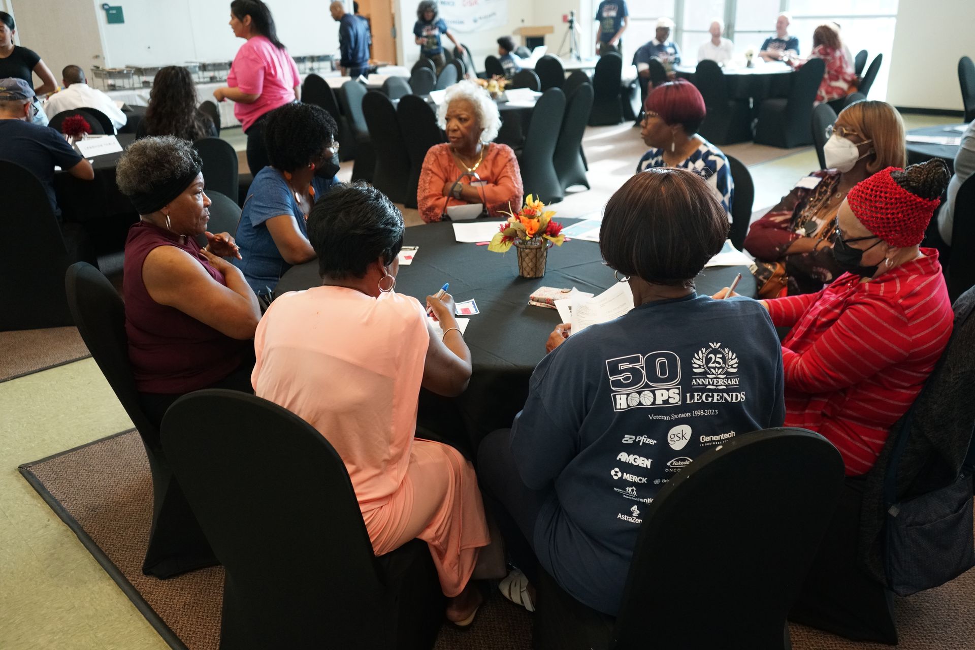 People seated around a black table, engaged in a group activity. Indoor setting with a few other people in the background.