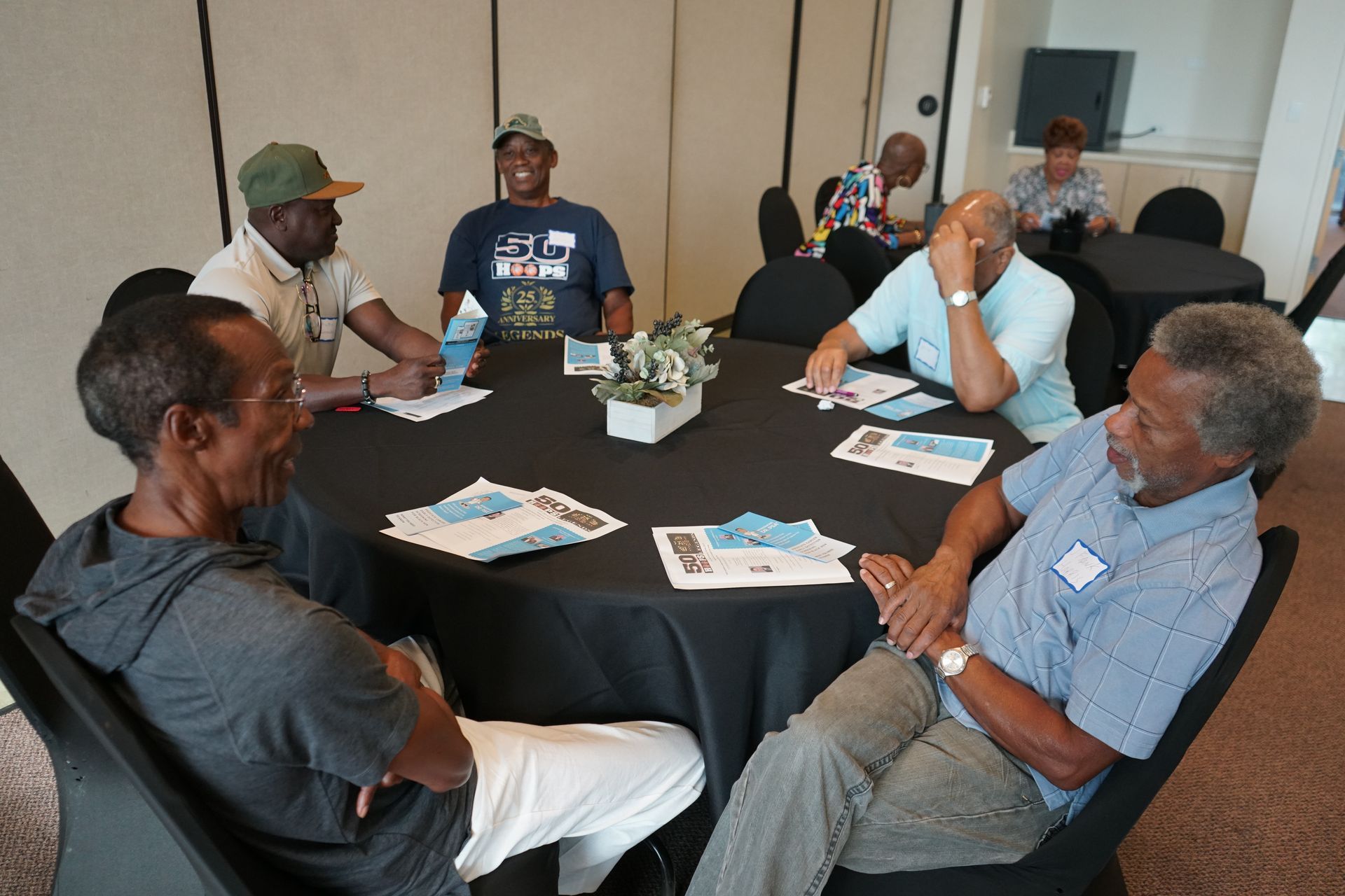 A group of people sitting around a black table in a meeting room, papers and a centerpiece on the table.