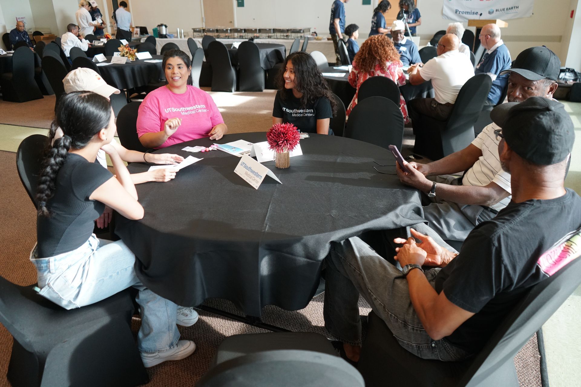 People sitting around a round table, engaged in conversation at an event; tables are covered in black.