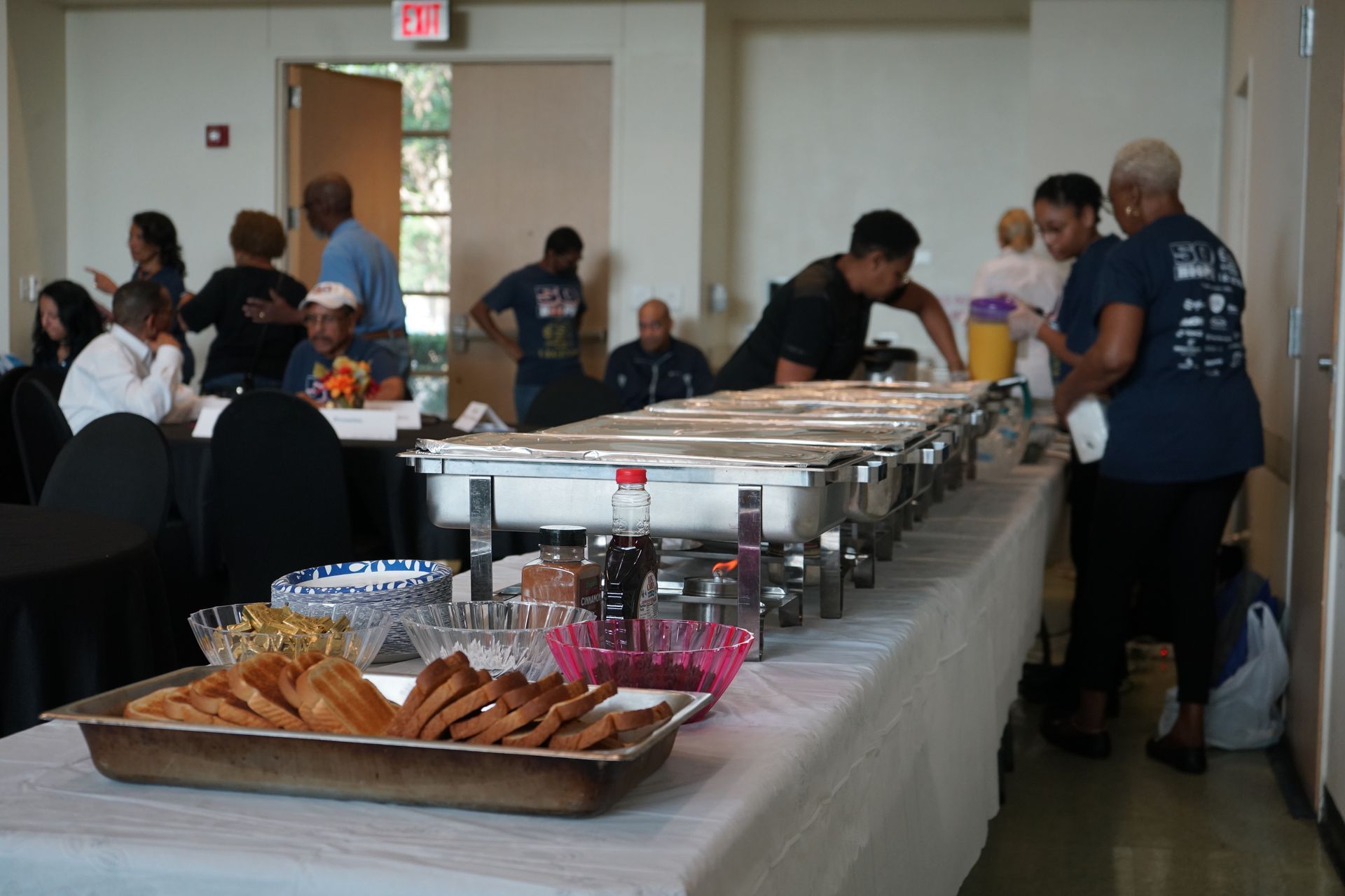 Buffet table with chafing dishes, food, and people.