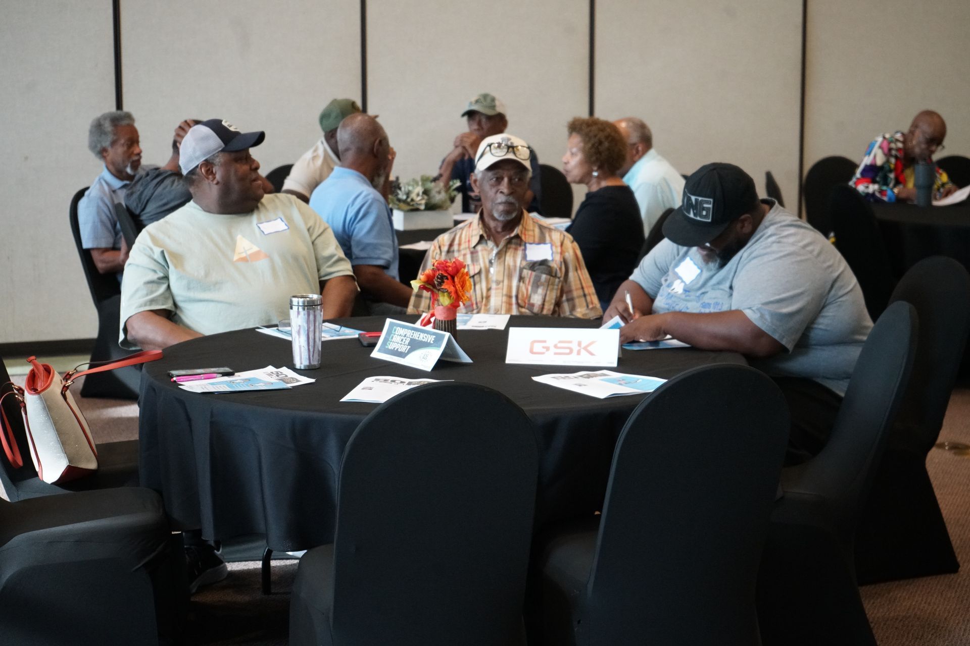 People seated around tables at a conference or meeting; black tablecloths and chairs.