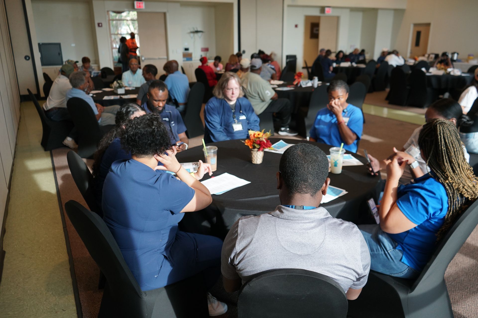 People seated around tables at a conference. Some are speaking and gesturing.