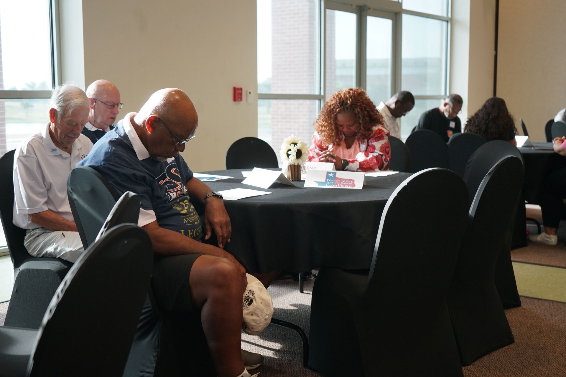 People seated around a table in a meeting room; some are looking down, others are writing.
