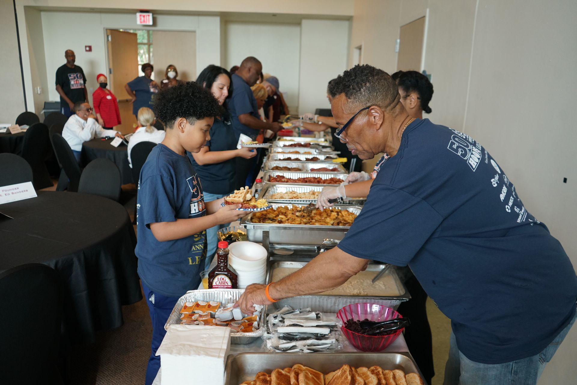 People serving themselves food from a buffet line. Various dishes are visible.