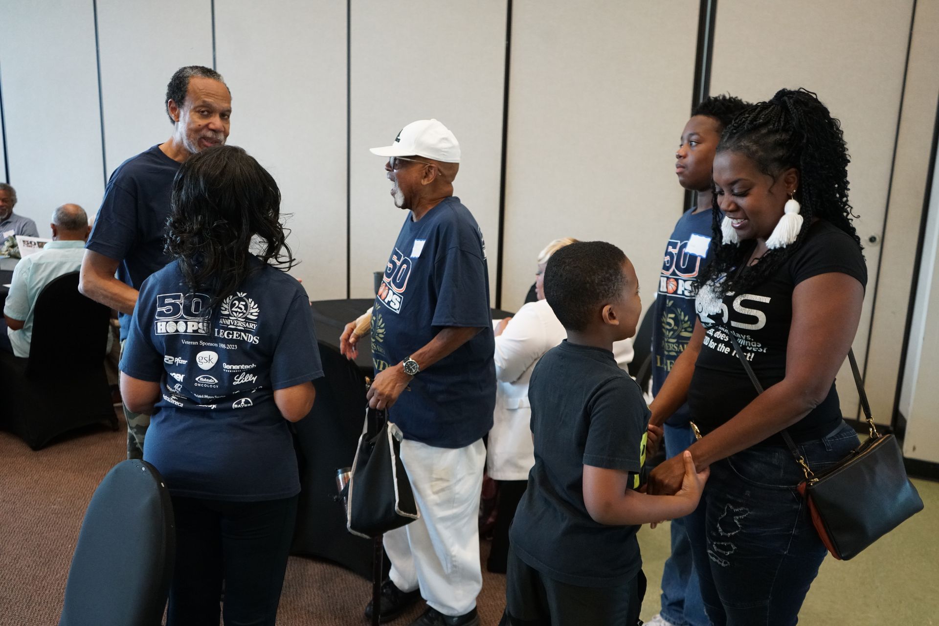 People in blue shirts and black pants converse at an indoor event.