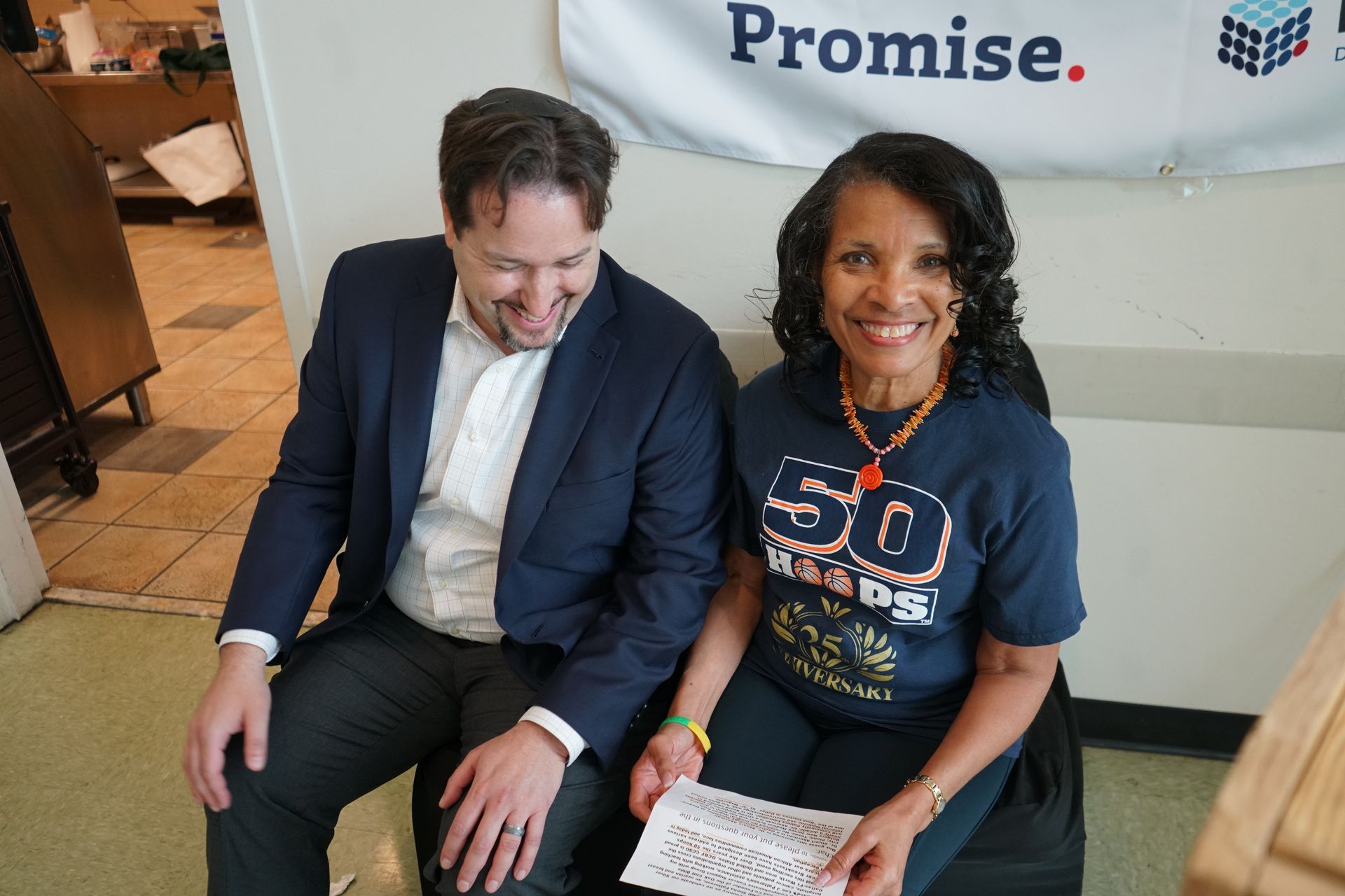 Man and woman smiling, sitting together. The woman wears a 