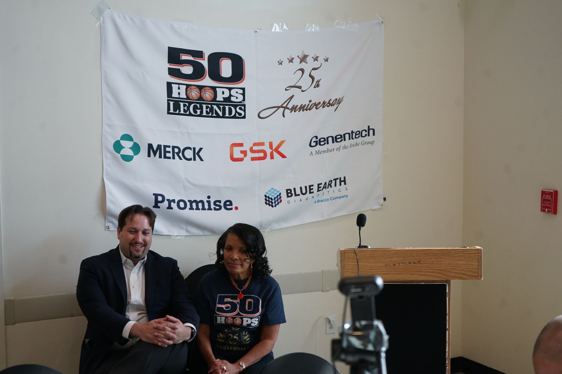 Man and woman seated in front of a banner for the 