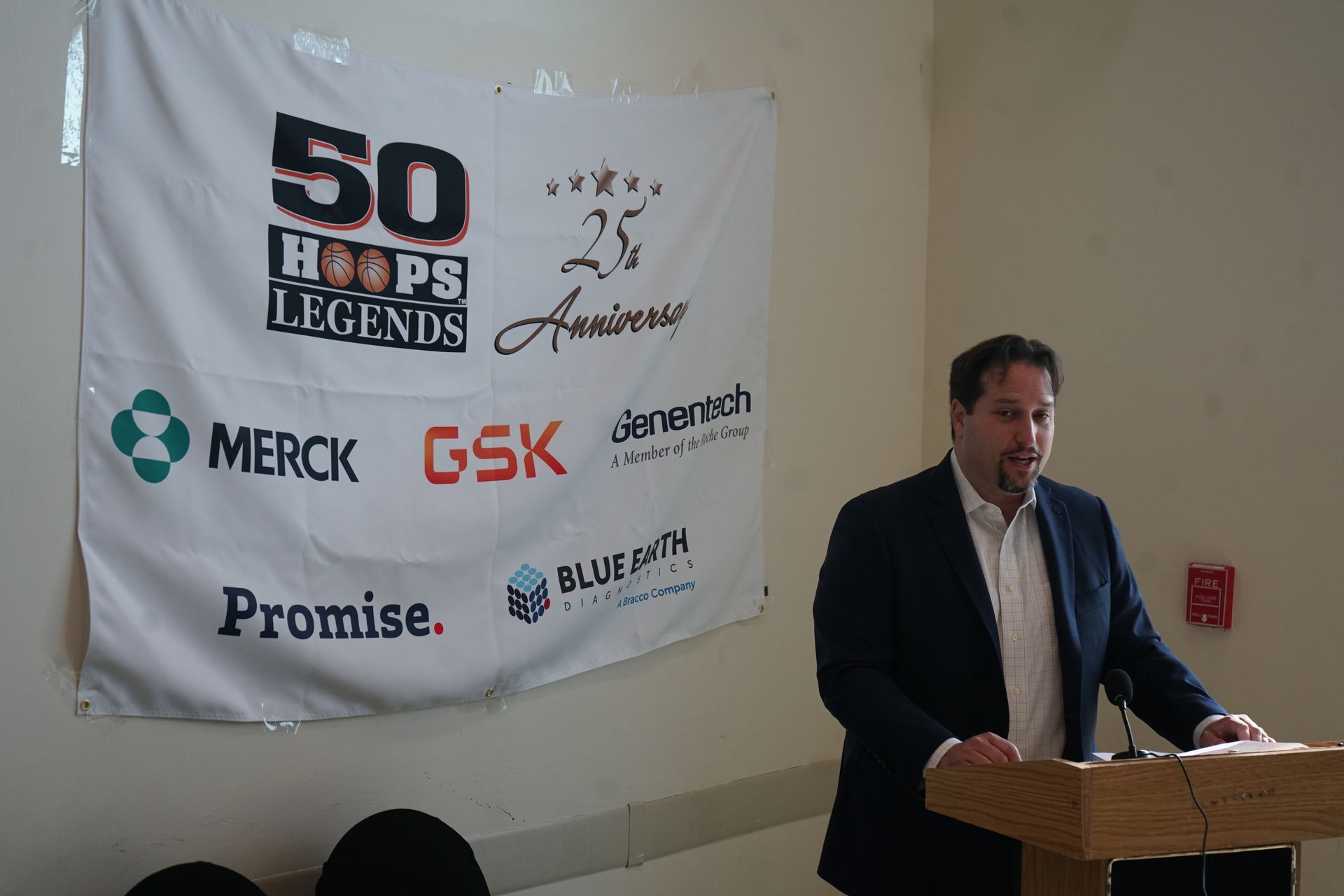 Man speaking at a podium in front of a banner for the 