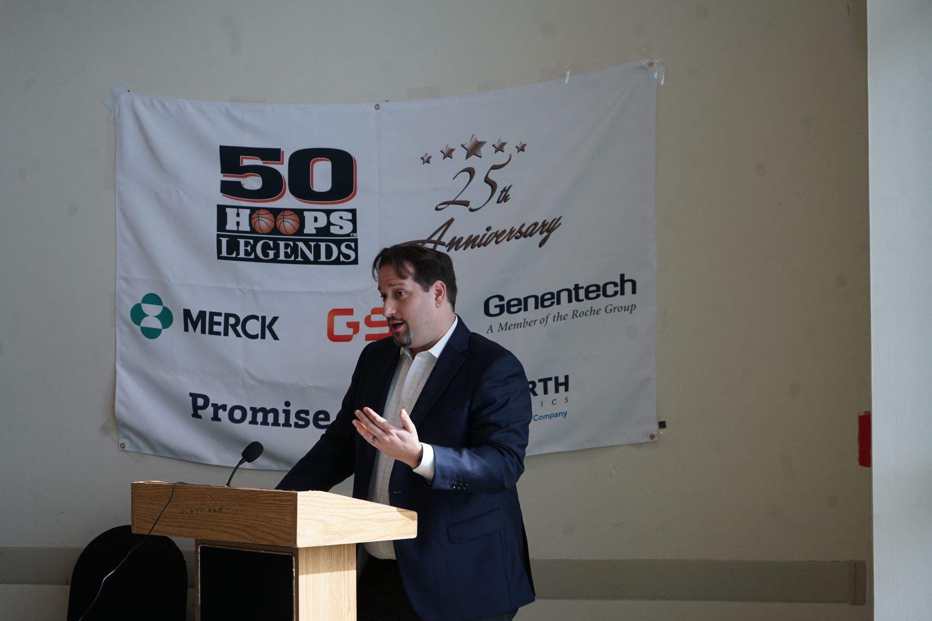 Man speaking at a podium in front of a banner for 