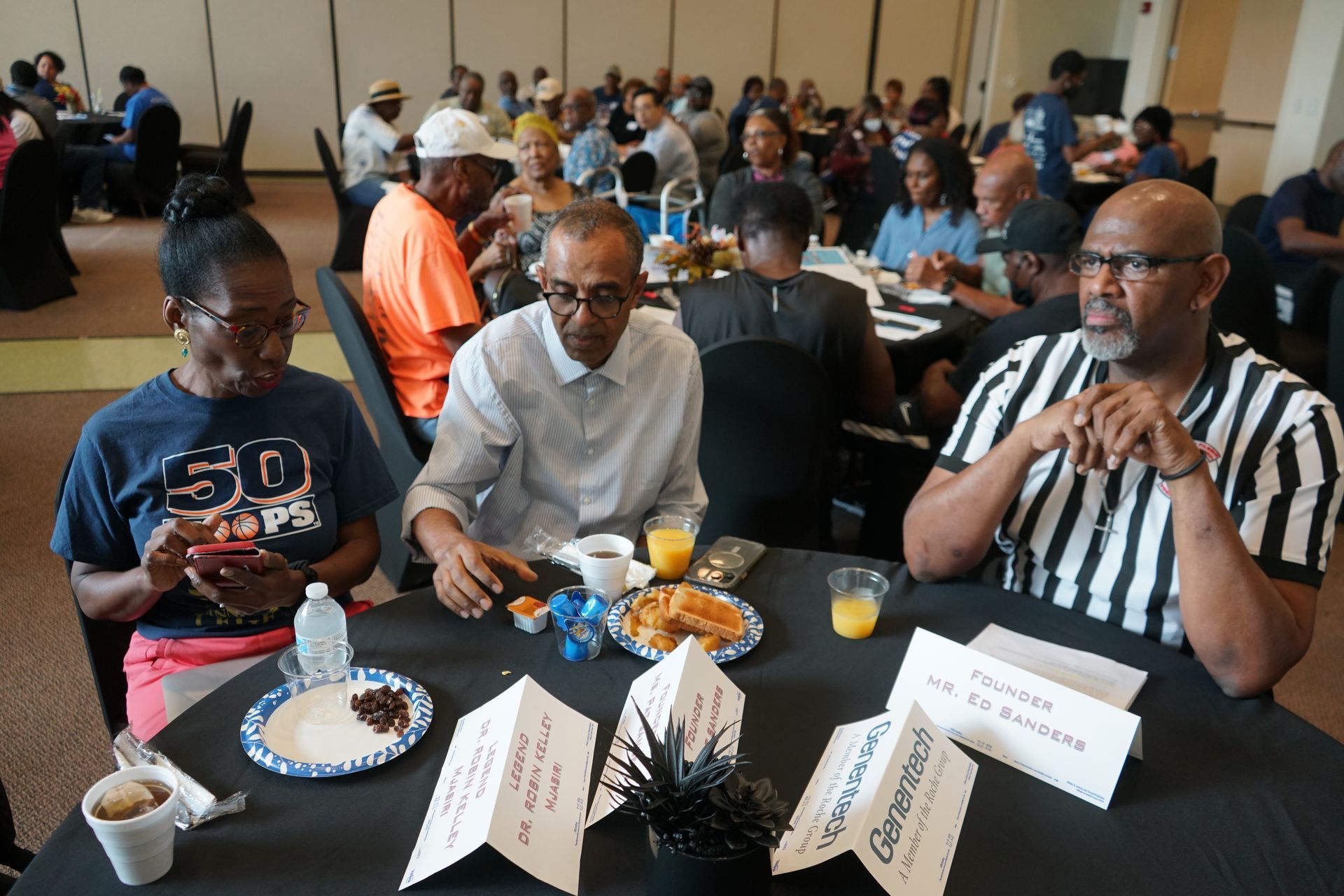 People at tables eating in a large room. Some have name cards.